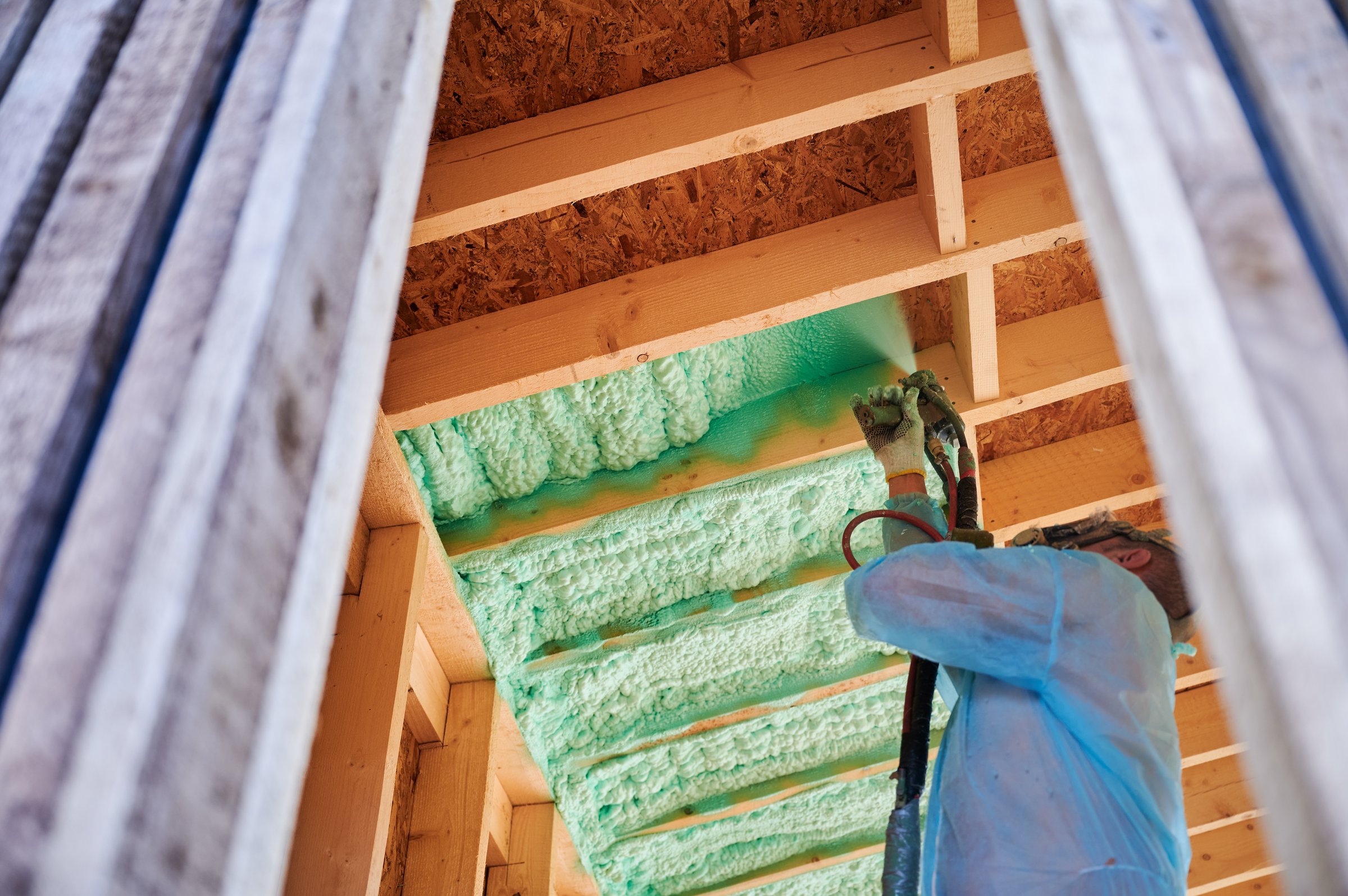 Male builder insulating wooden frame house. Man worker spraying polyurethane foam inside of future cottage, using plural component gun. Construction and insulation concept.