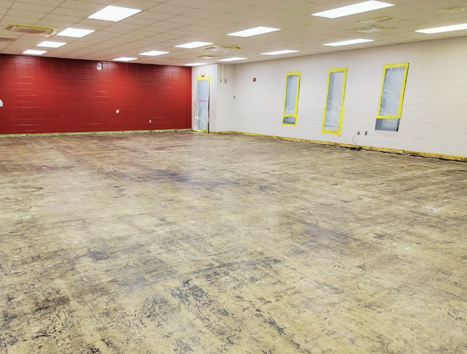 A large indoor space being renovated with a red ladder, exposed flooring, and a floor polishing machine in the center.