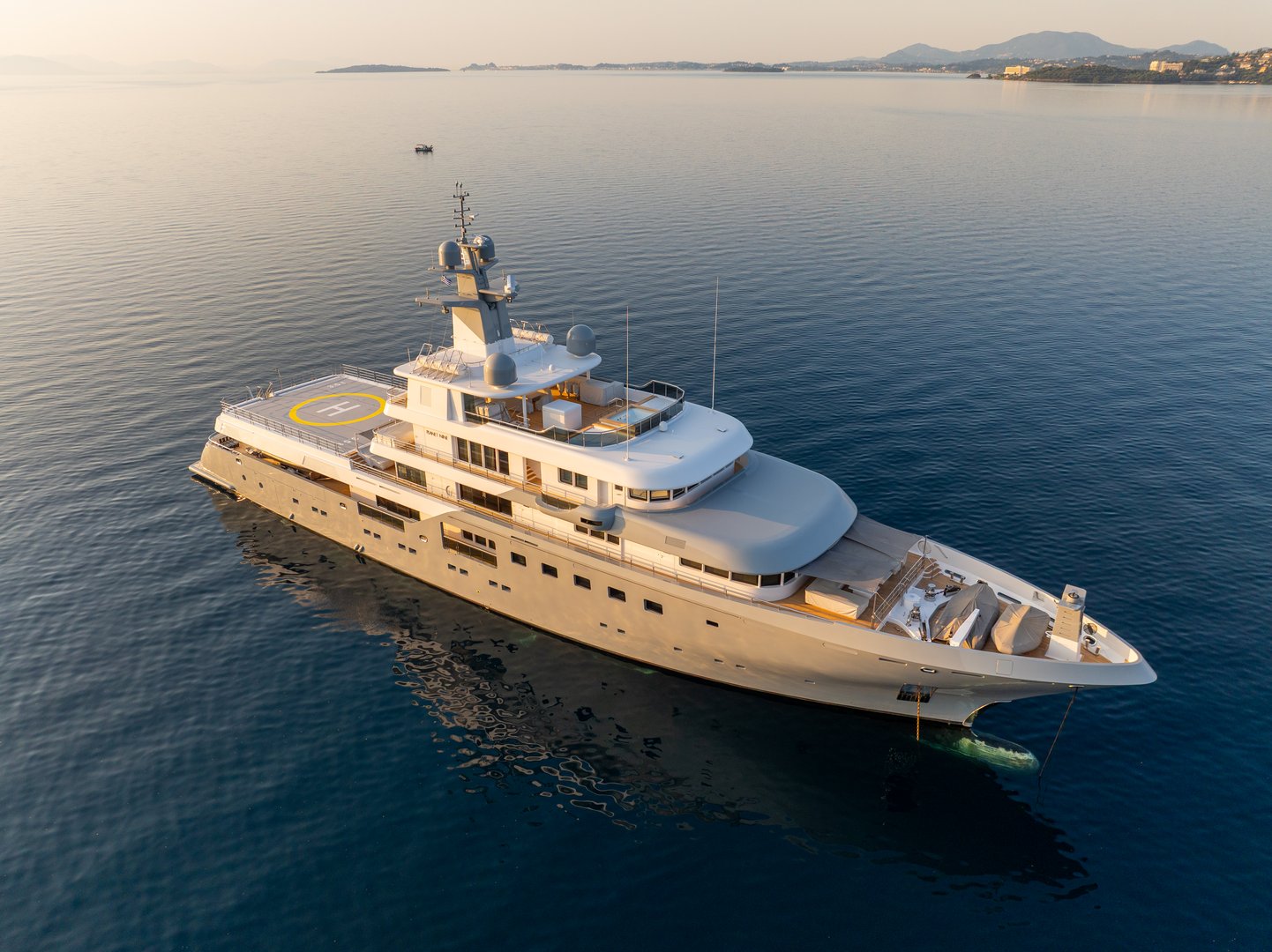 Aerial drone view of a luxury superyacht with a helipad, anchored in a calm turquoise bay at sunrise. A symbol of wealth, travel, and exclusive lifestyle in a beautiful mediterranean location