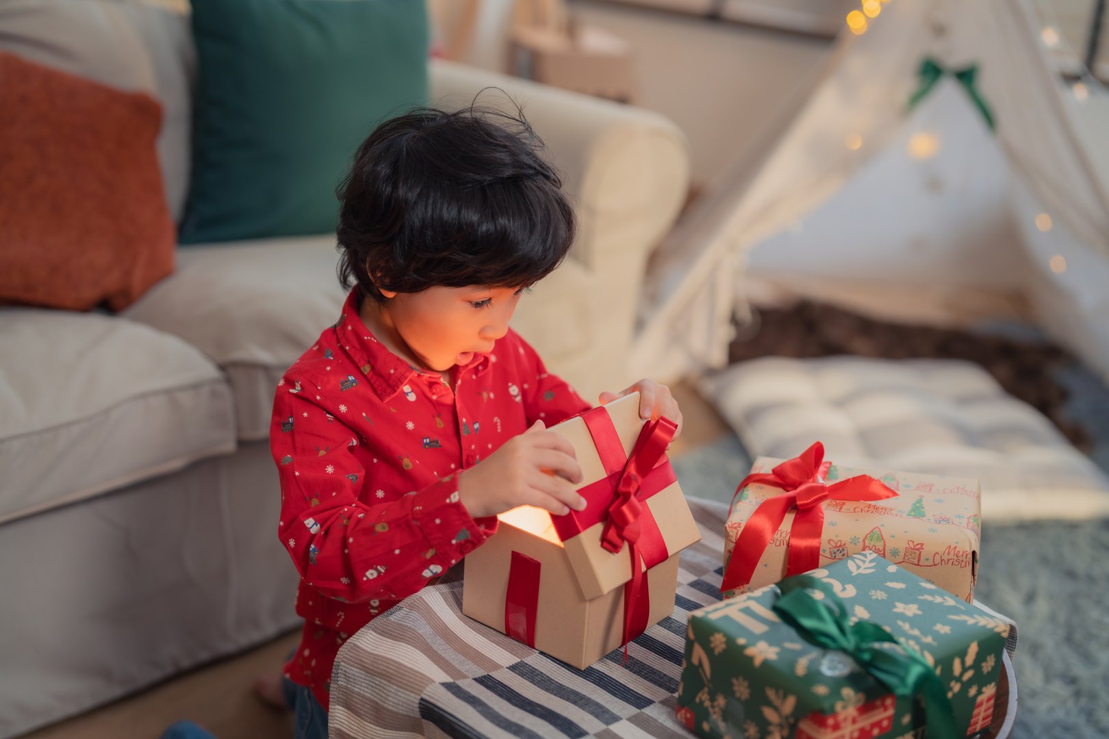 A joyful child opens gift box during festive holiday celebration, surrounded by beautifully wrapped presents and cozy living room atmosphere.