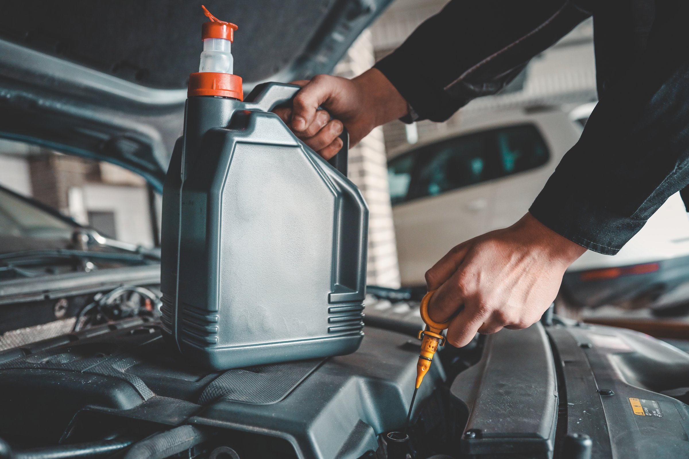 Close-up of a mechanic holding a bottle of motor oil and an oil dipstick, performing an oil change in a vehicle. Highlights car maintenance and servicing tasks.