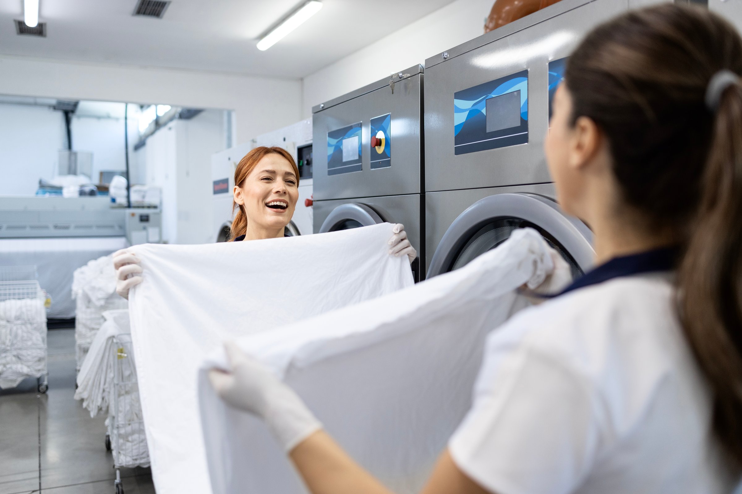 Female workers folding clean laundry after washing in dry cleaning company.