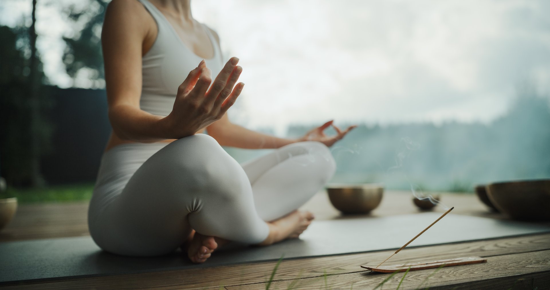 Anonymous Female Sits Cross-Legged, Meditating in a Nature Retreat, Blending with Peaceful Forest Surroundings. Incense Gives Soothing Aromas, while the Harmonious Tones of Singing Bowls Resonate