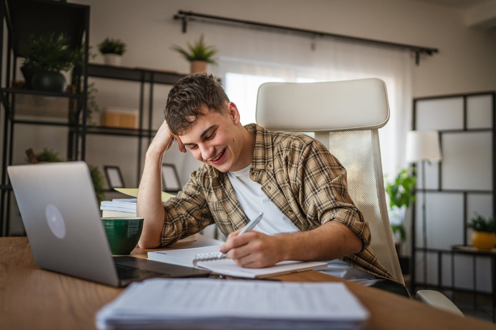 young man student learn and prepare exam write details at notebook and use laptop at home