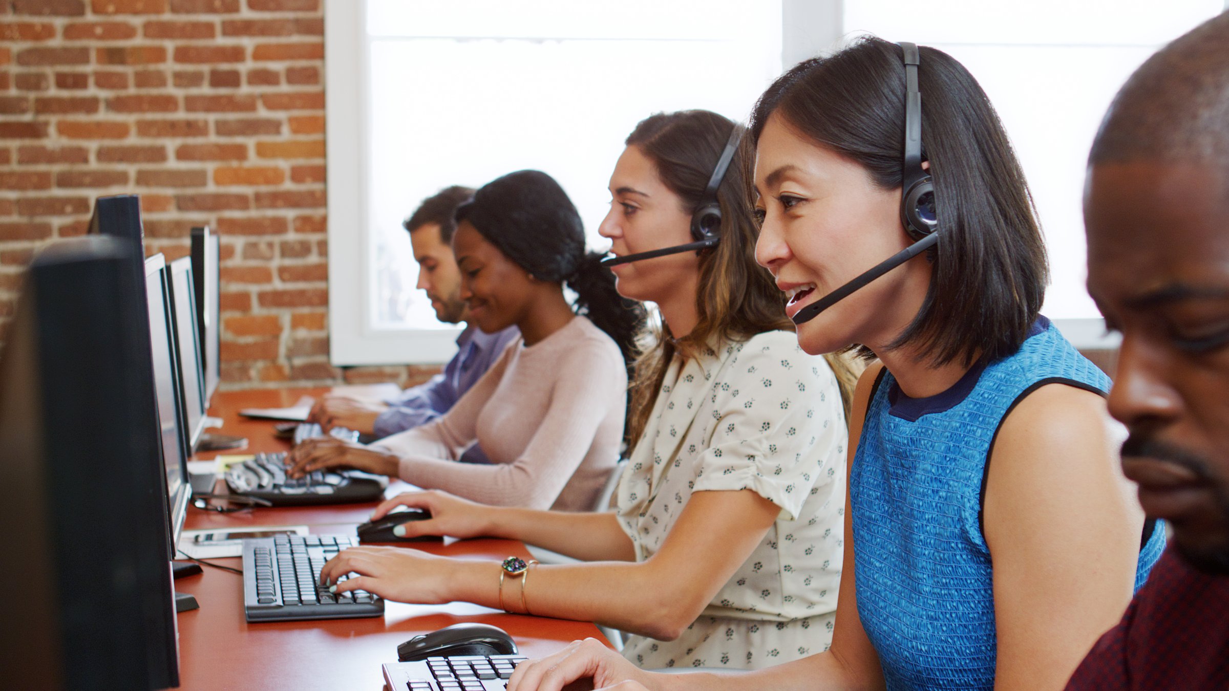 Multi-Cultural Business Team Wearing Headsets Working In Busy Customer Service Department