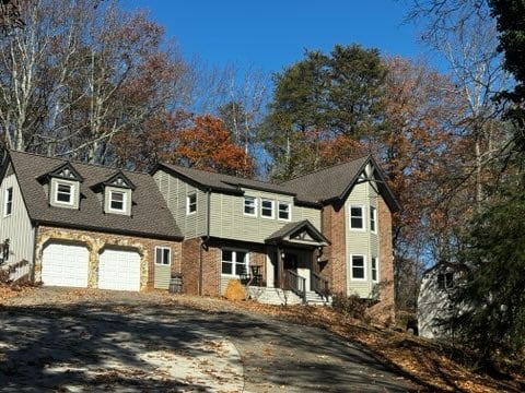 Two-story brick and siding house with a gray roof, double garage, and surrounding autumn trees under a clear blue sky.