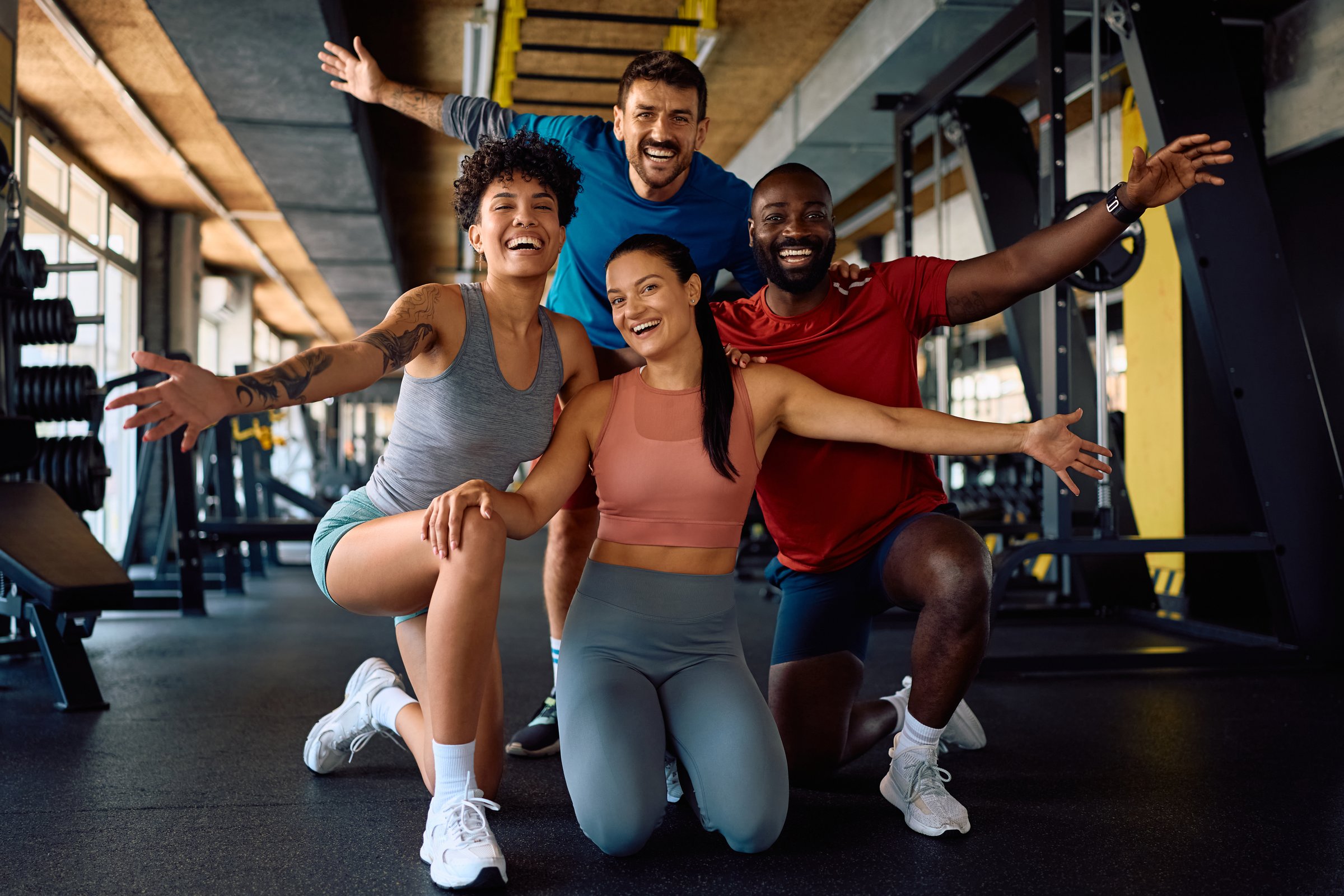Happy athletes with arms outstretched having fun during gym workout and looking at camera.