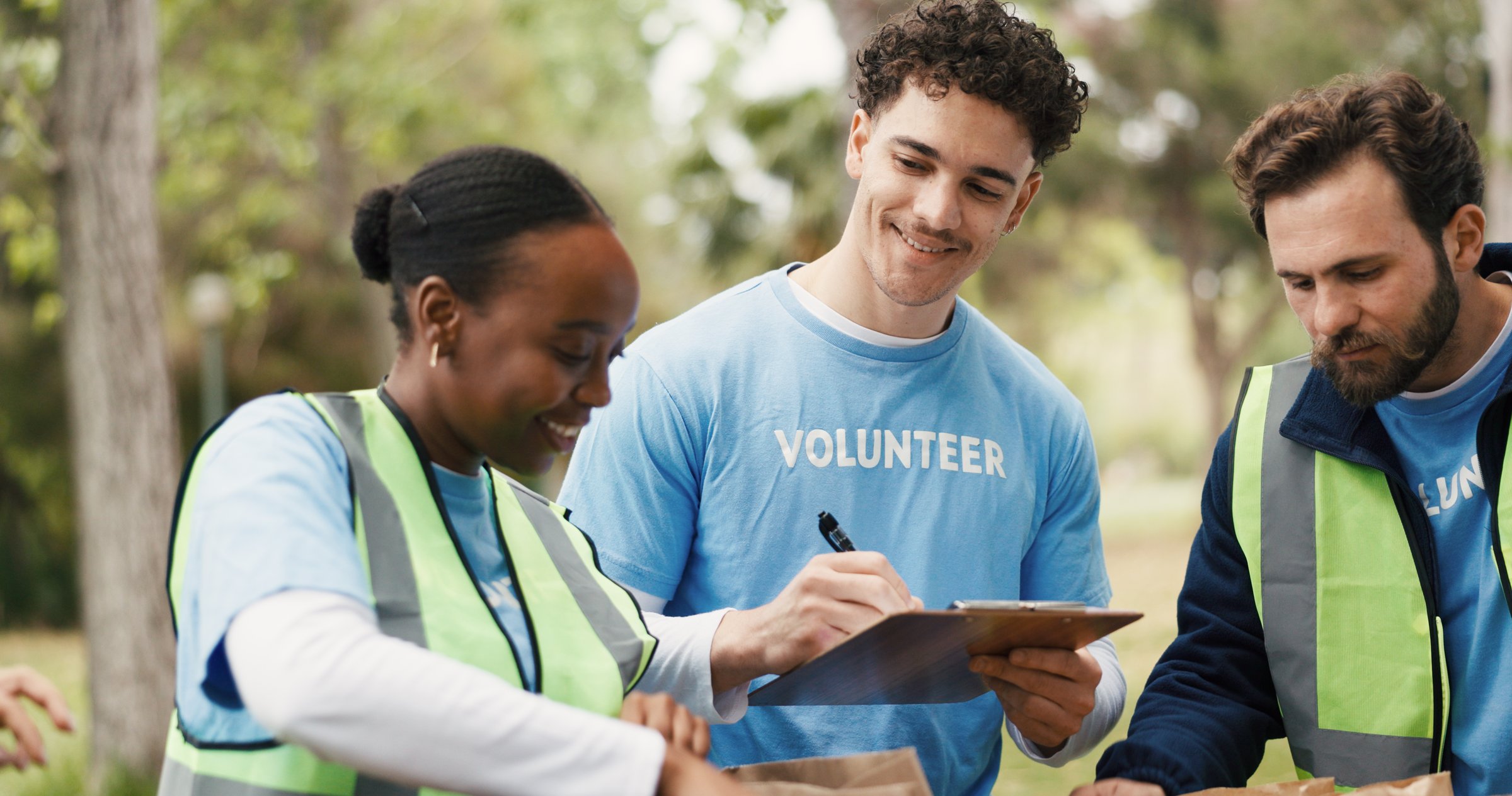 Checklist, volunteer and people with in park for food drive, community service and packaging for charity event. Teamwork, local ngo and man check donation supply with clipboard, paper bag and outdoor