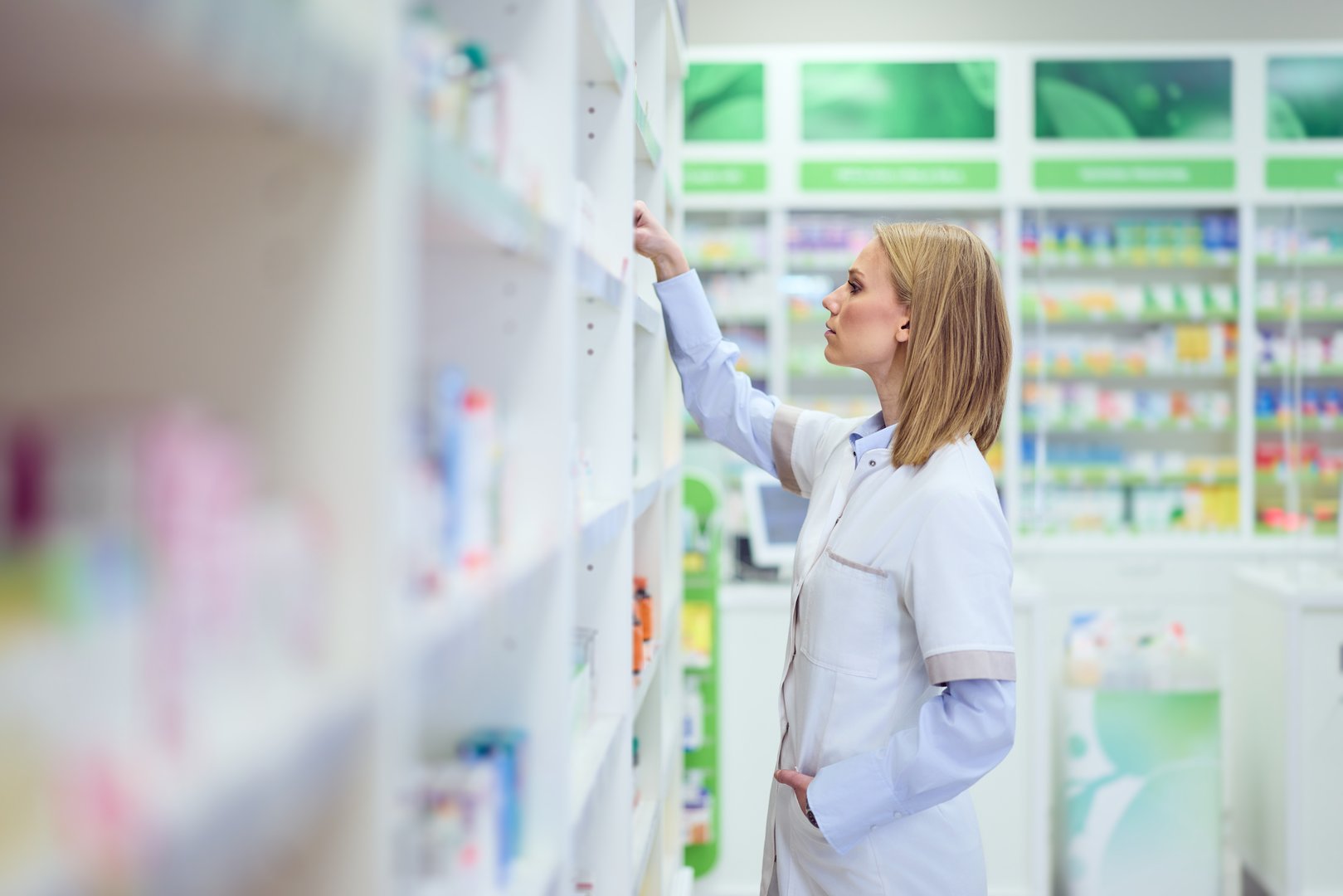 Pharmacist organizing products on shelves in a brightly lit pharmacy interior.