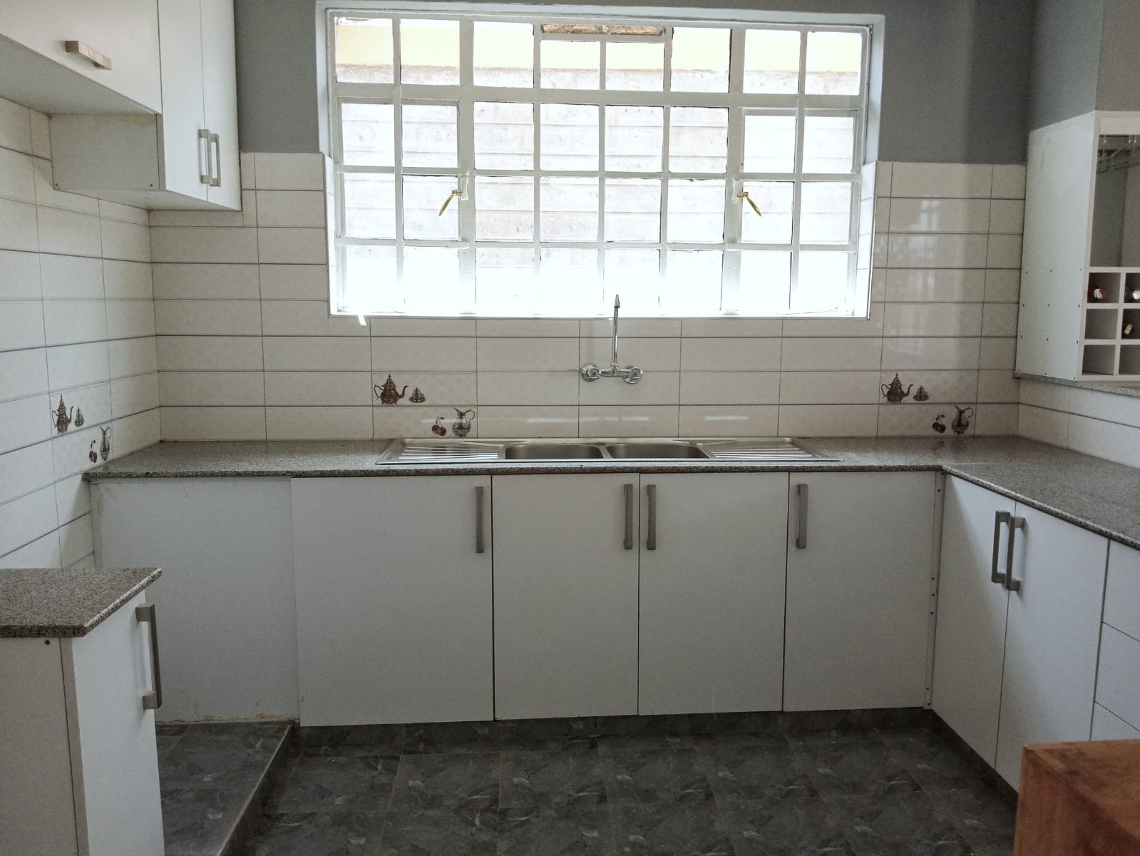 Minimalist white kitchen with tiled backsplash, gray countertops, and large window above a double sink.