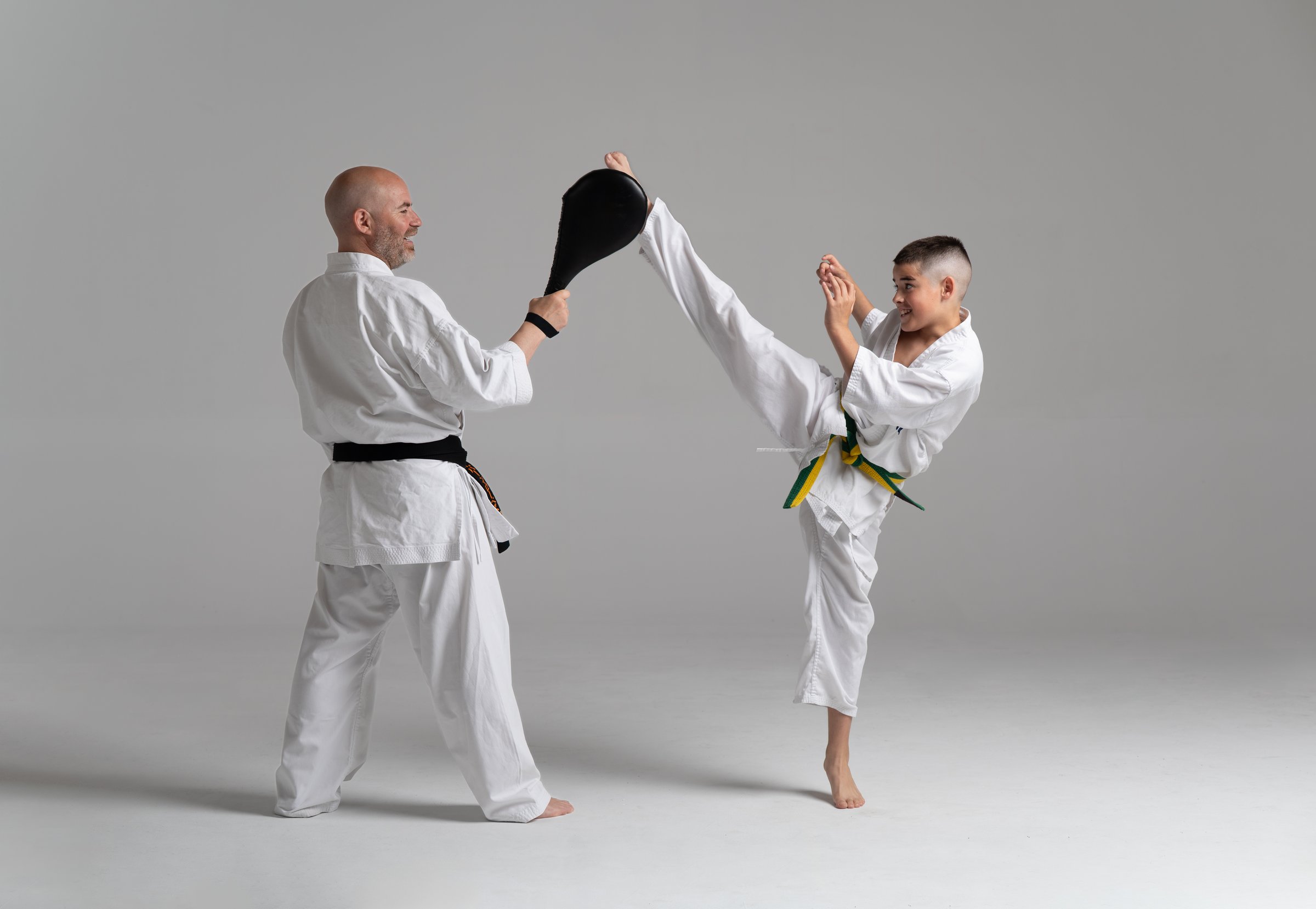 Young karate student practicing a kick on a pad held by his instructor, during a kyokushinkai training session