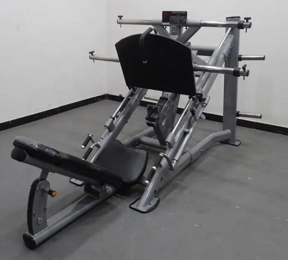A leg press machine in an empty gym room with a padded seat and metal frame, designed for lower body strength exercises.