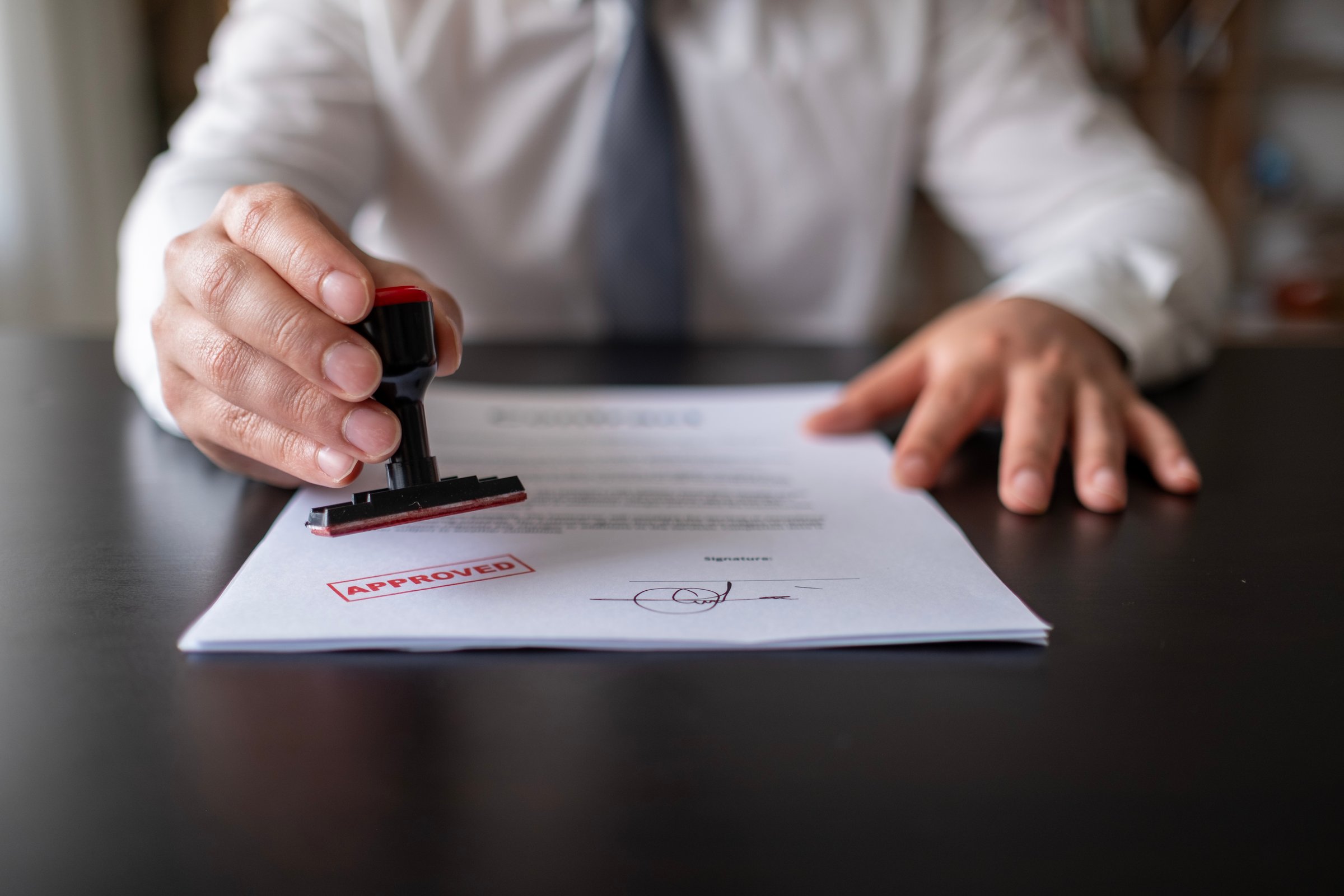 Real estate trade real estate agent employee holding puts stamp for sale approval. Businessman or notary public stamping approved stamp on document in meeting.