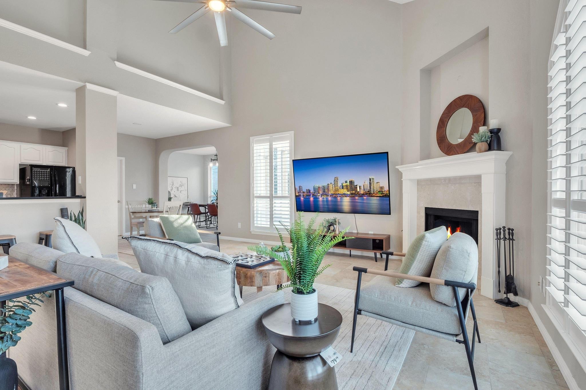 Modern living room with gray couches, TV above fireplace, and large windows with shutters.