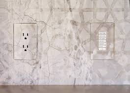 A wall with a modern electrical outlet and a multi-button control panel, both set against a textured, light gray surface.