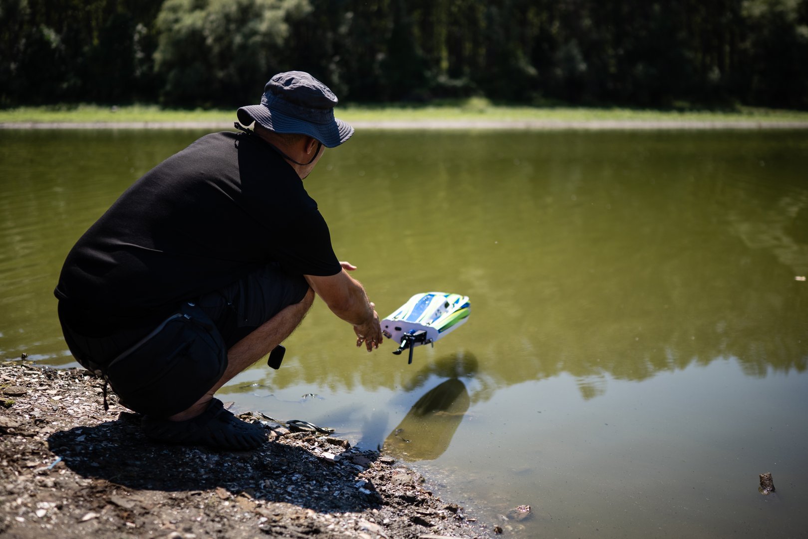 Man launches a remote-controlled boat into a lake on a sunny summer day, enjoying his hobby outdoors