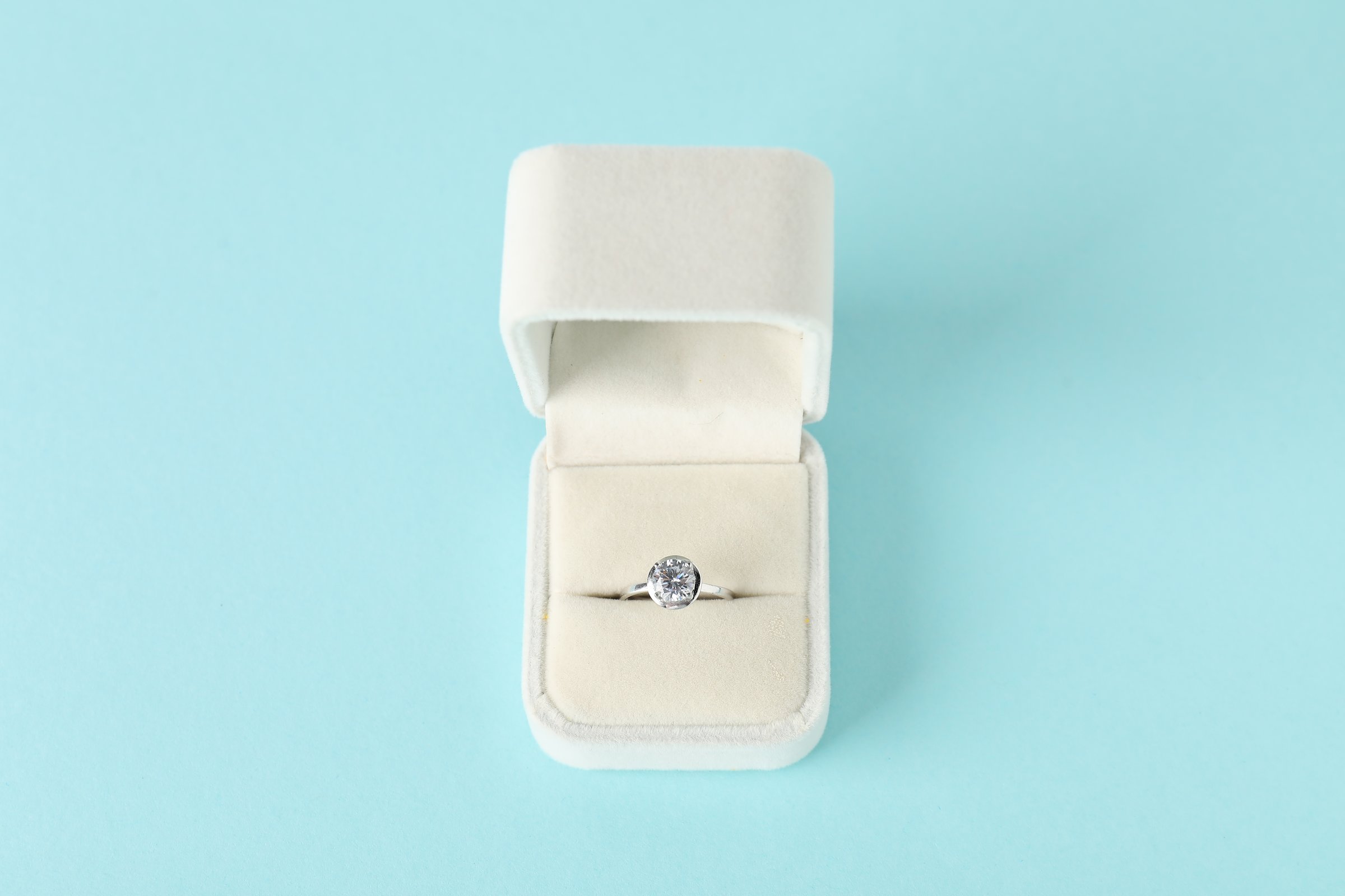 Beautiful ring with gemstone in box on light blue background, above view