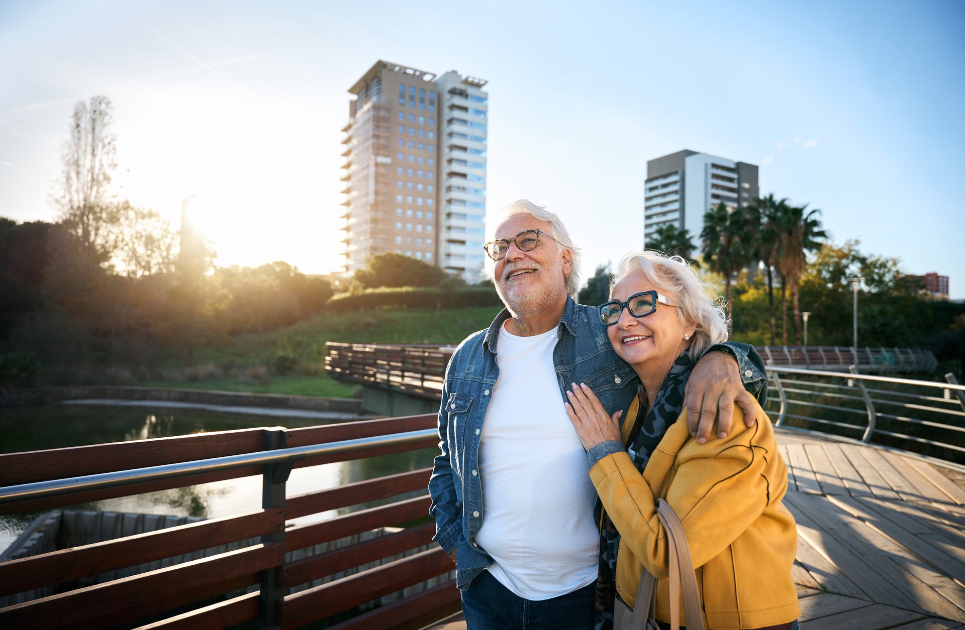 Senior couple walking arm in arm, smiling at sunset in a city park, enjoying a romantic and peaceful moment surrounded by nature and the warm golden light of the day coming to an end