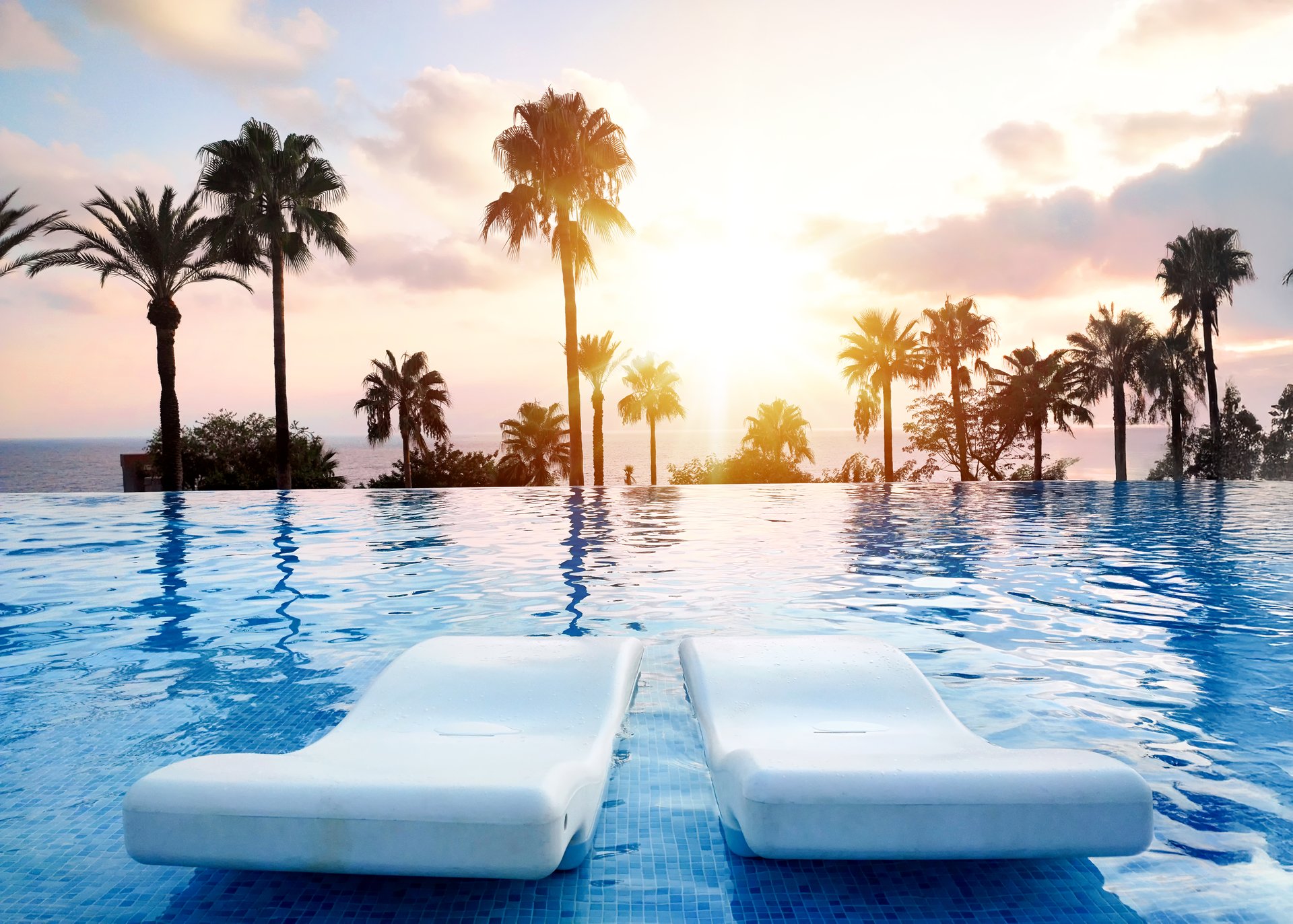A tranquil sunset view over an infinity pool with palm trees, ideal for relaxation and vacation tropical themes.