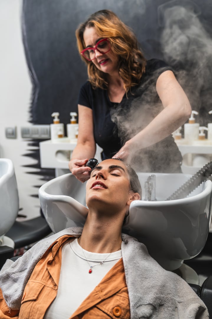 Hair stylist applying a steam treatment to a client's hair at the wash basin in a professional salon