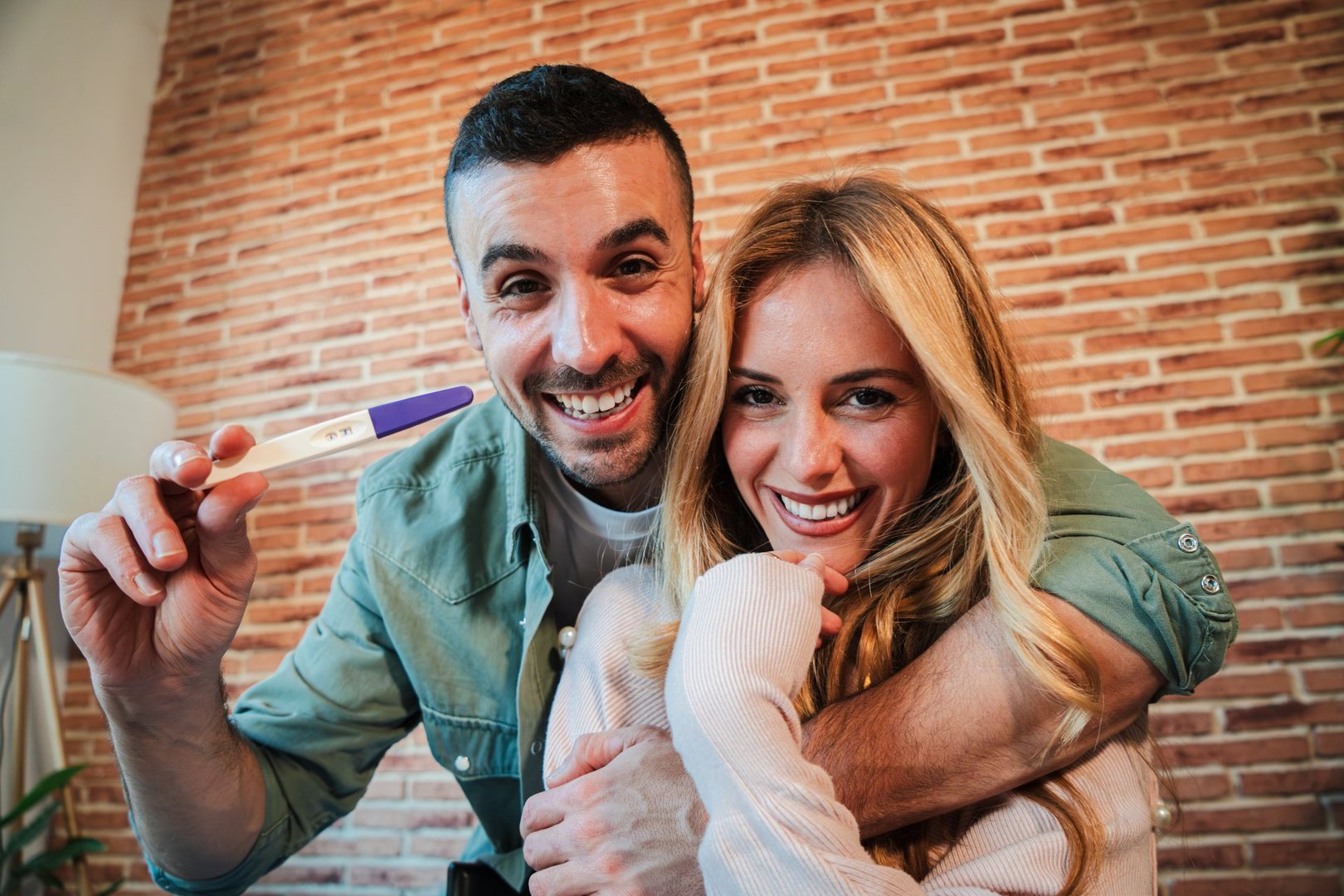 Excited couple celebrating positive pregnancy test, embracing and smiling together at home, sharing joyful news of expecting a baby, expressing happiness and anticipation for their new family journey. High quality photo
