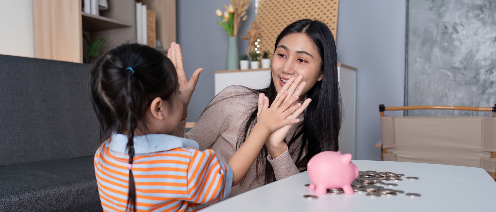 A mother and daughter celebrate financial milestones with high fives, focusing on the concept of savings. Parenting emphasizes fun and financial oaths.