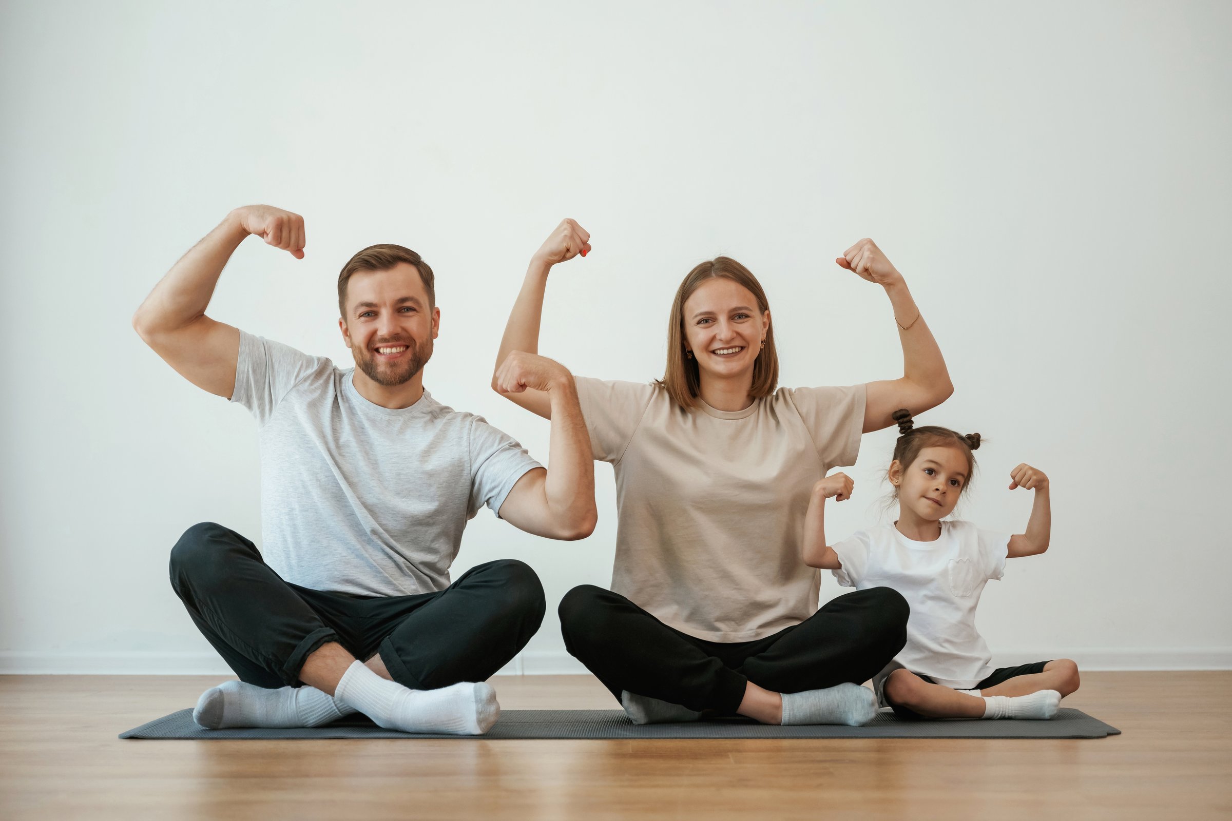 Showing the biceps, strong. Family of mother, father and daughter are doing yoga at home.