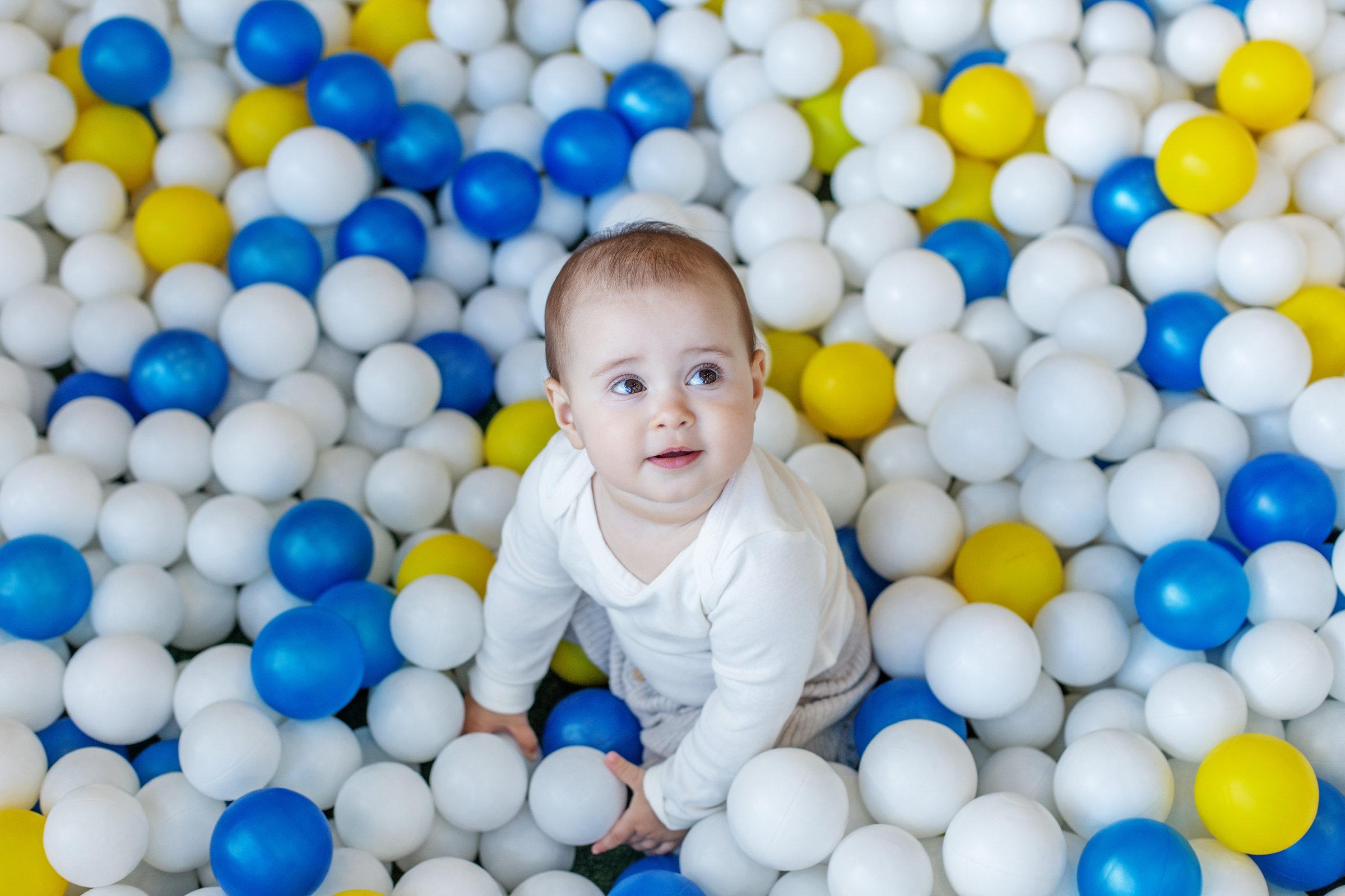 Top-down view of a smiling baby playing in a vibrant indoor ball pit