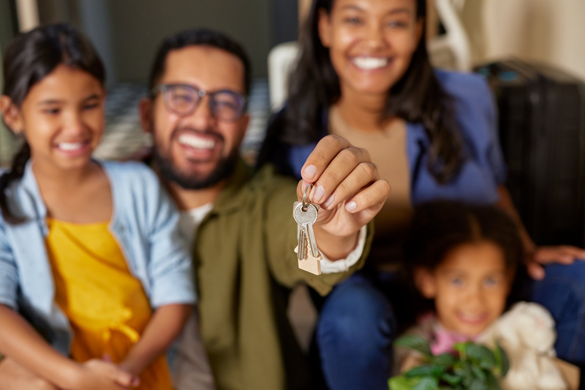 Close up of happy father hands holding new house keys while sitting with family. Happy family excited on purchasing new house with her daughters. Beautiful hispanic couple feeling excited to shift to new house.