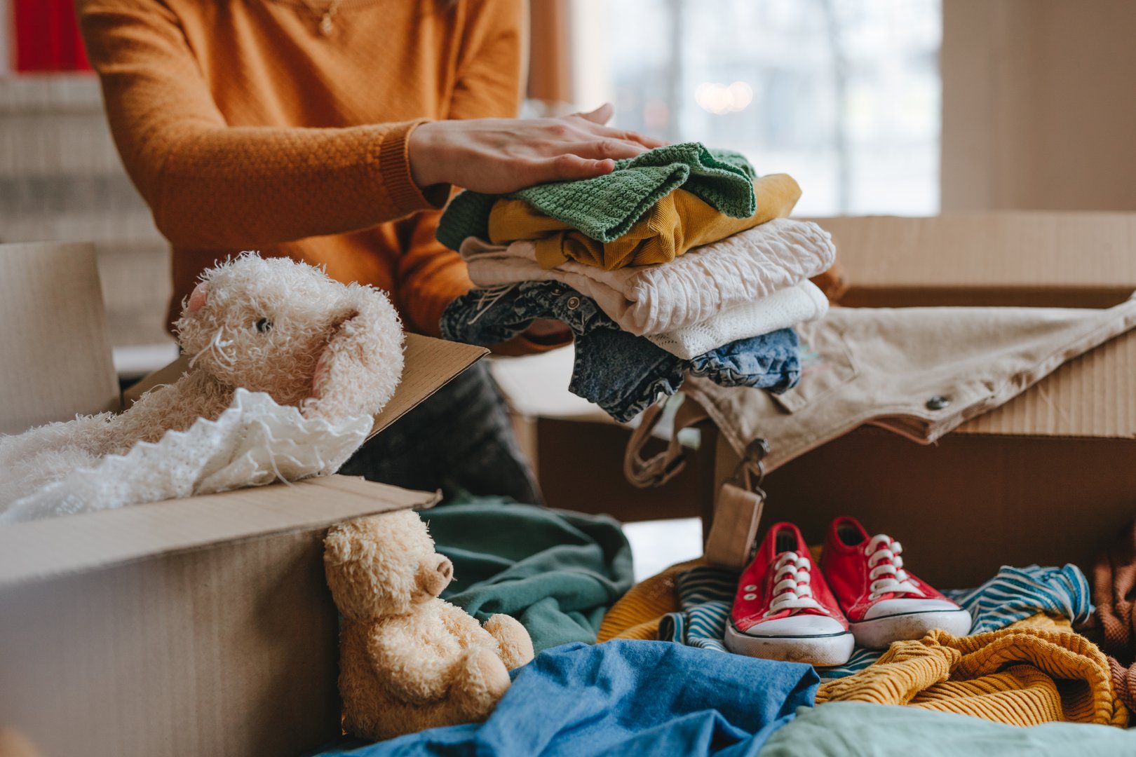 Close-up of woman sorting an old out-of-use kid toy, clothes and shoes in box for charity or converting discarded materials. Upcycling concept.
