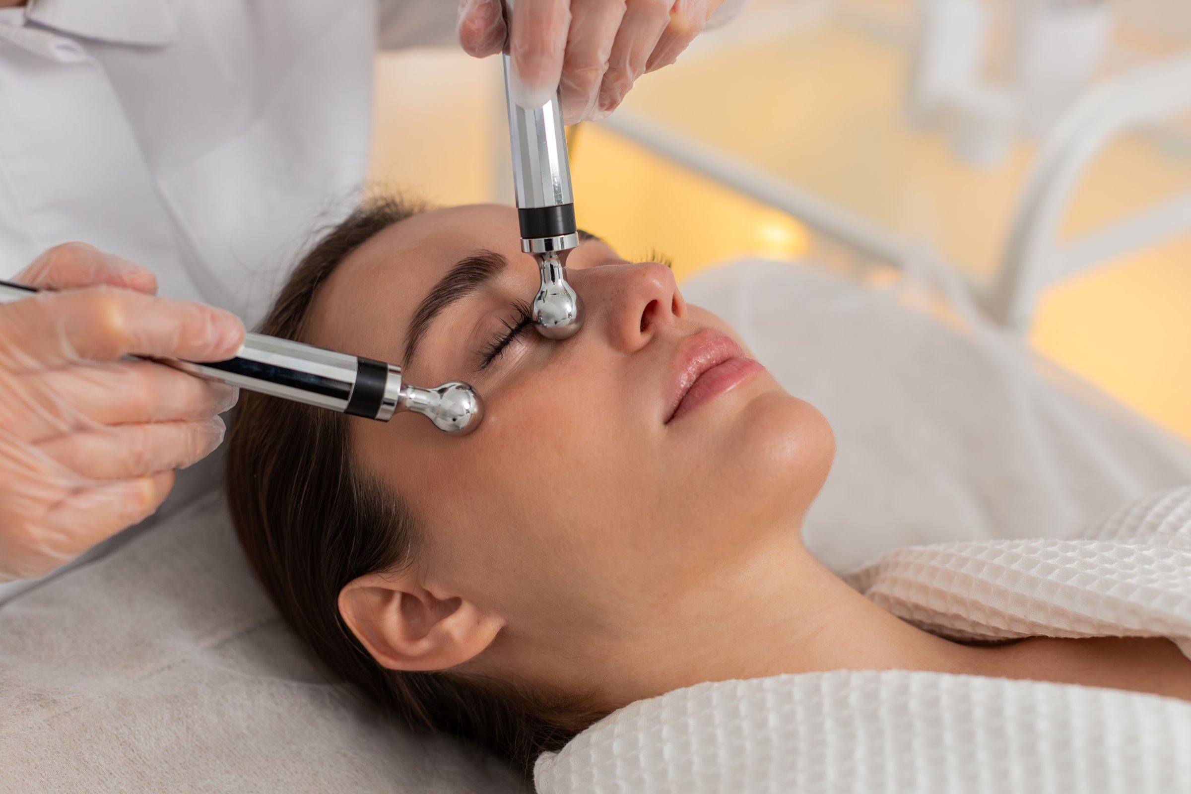Cosmetologist doctor makes woman micro currents face cheek therapy. Girl skin care anti-age in spa clinic. Beautician using electrical impulses for facial cosmetic beauty treatment procedure.