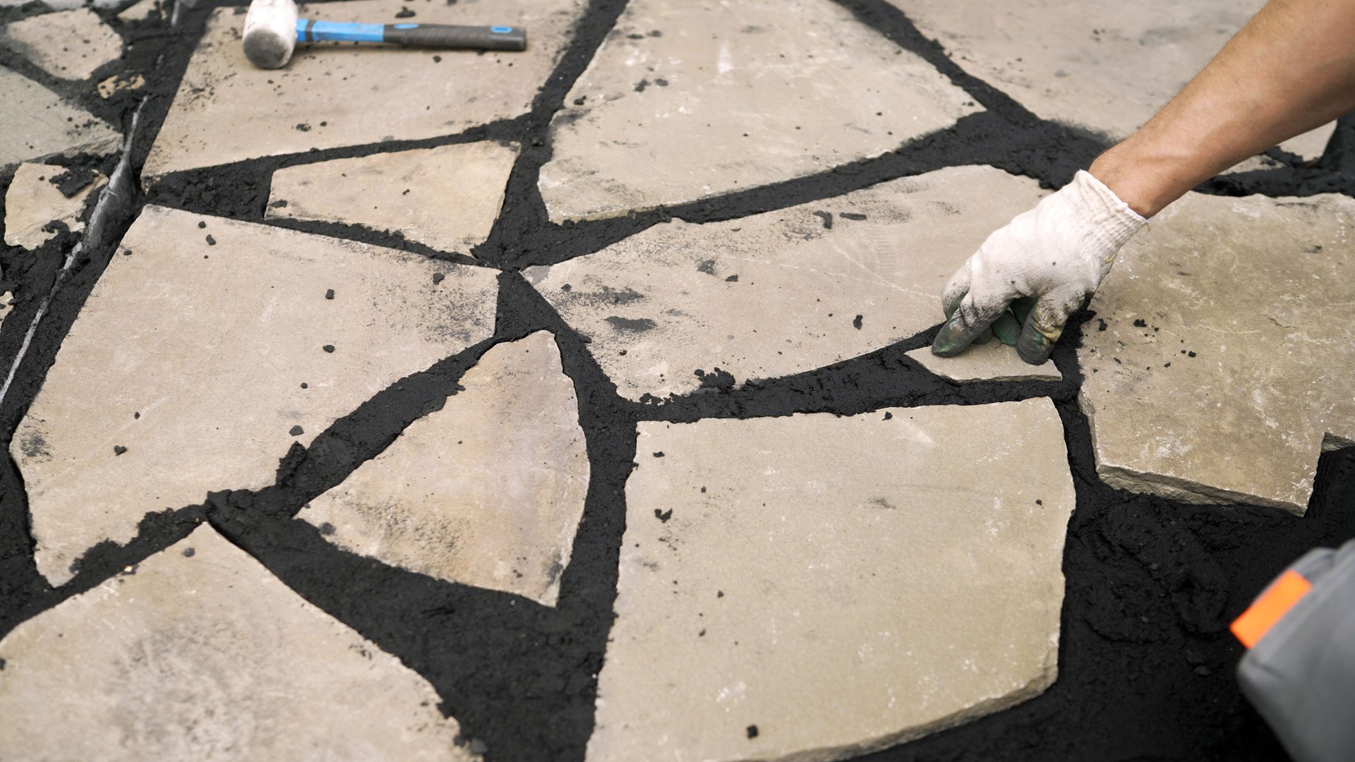 Professional construction worker brushing excess grout from newly laid flagstone patio during meticulous outdoor landscaping installation process