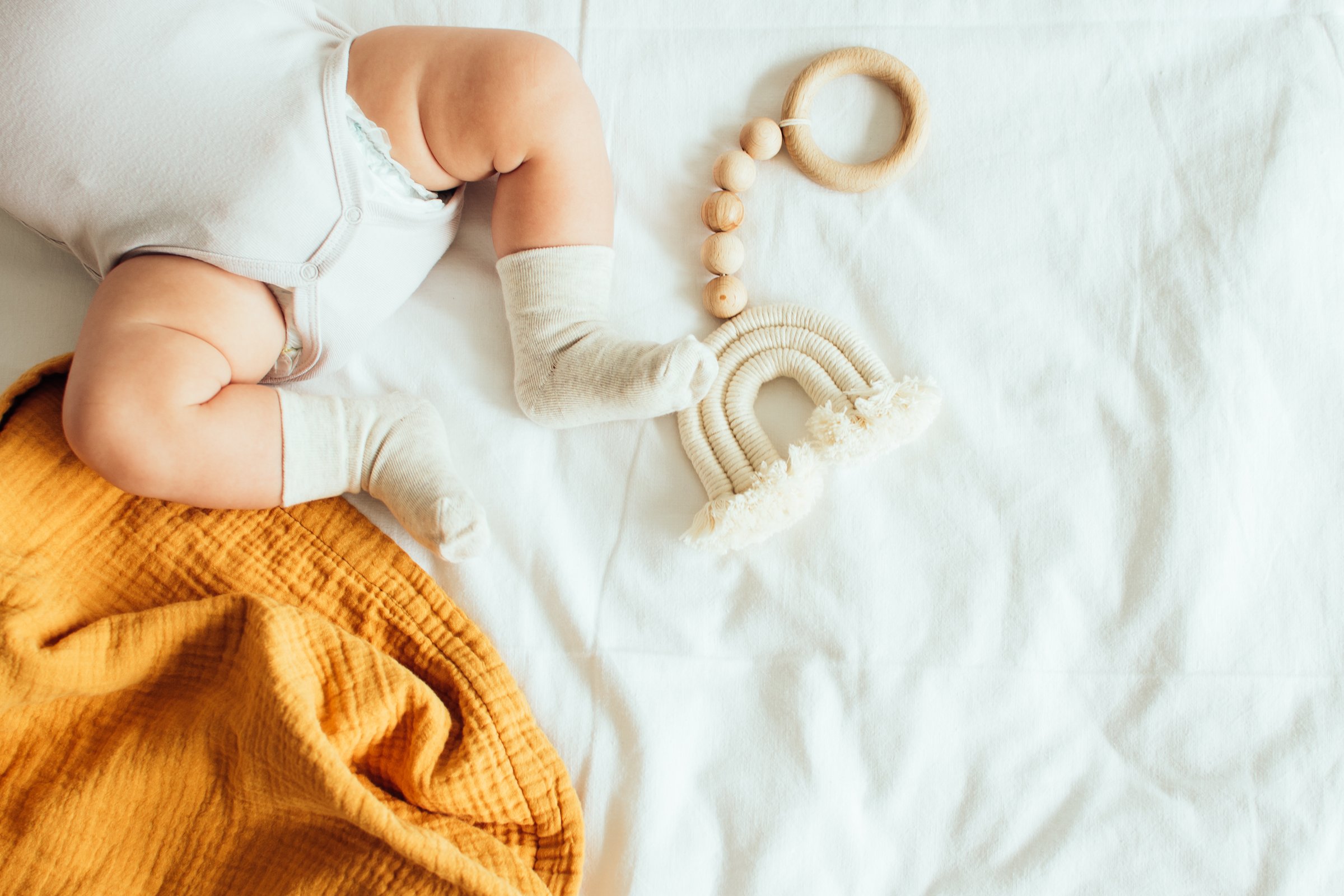 Baby playing with a wooden toy on white linens background. Top view. Copy space.