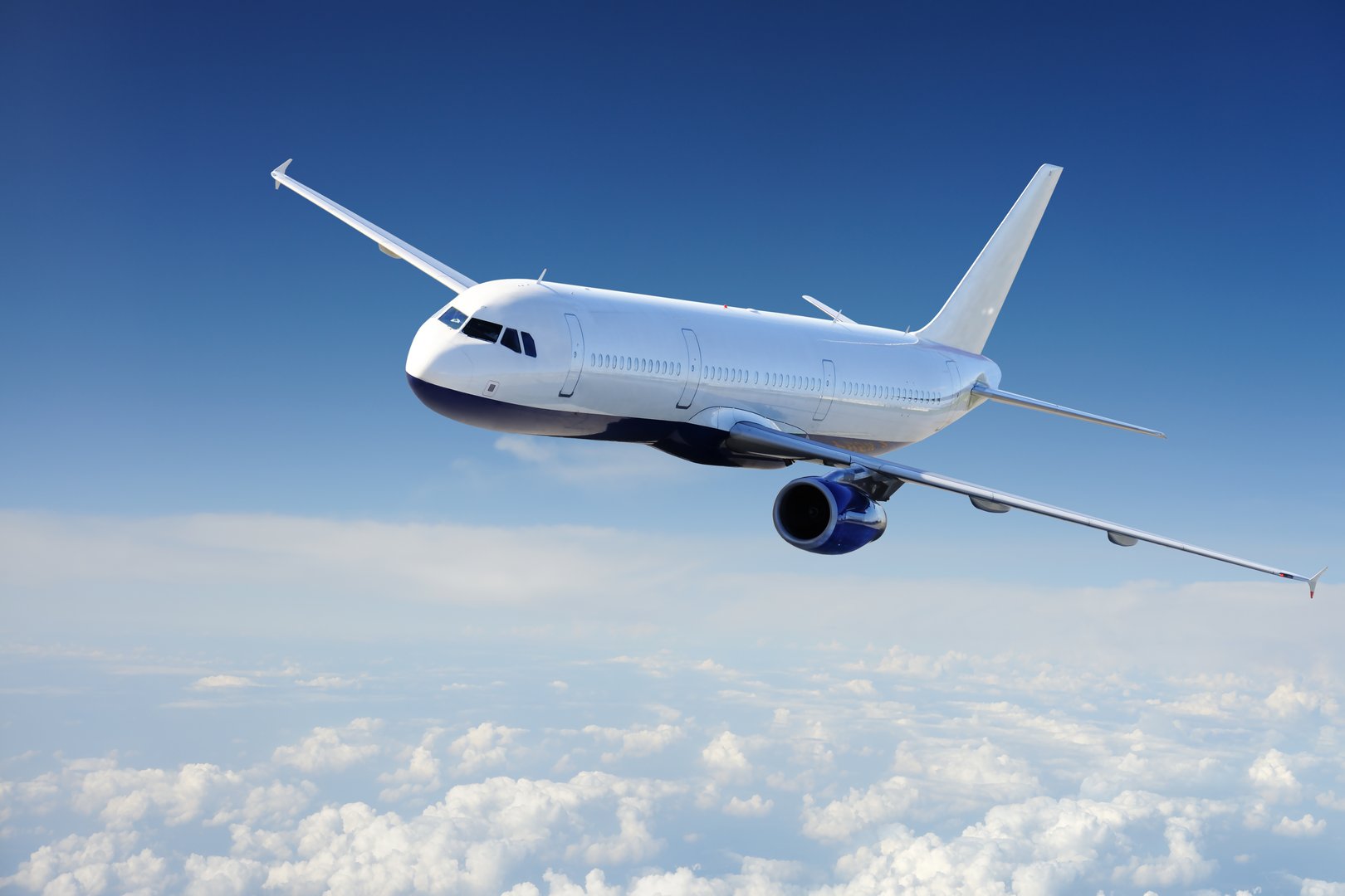 Commercial airplane flying above clouds against a clear blue sky.