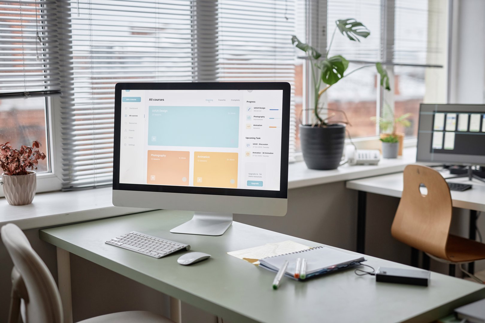 Background shot in pastel colors of office workplace table with computer monitor displaying page with online education courses. Room is cozy and full of light