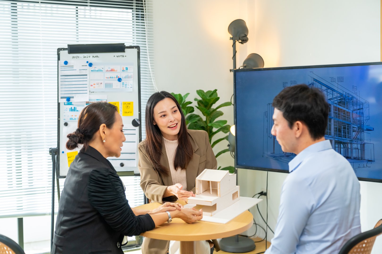 Group of Asian Architects and department manager teamwork meeting discussion and presentation 3D architectural displayed model of energy efficient and sustainability home design in office conference room.