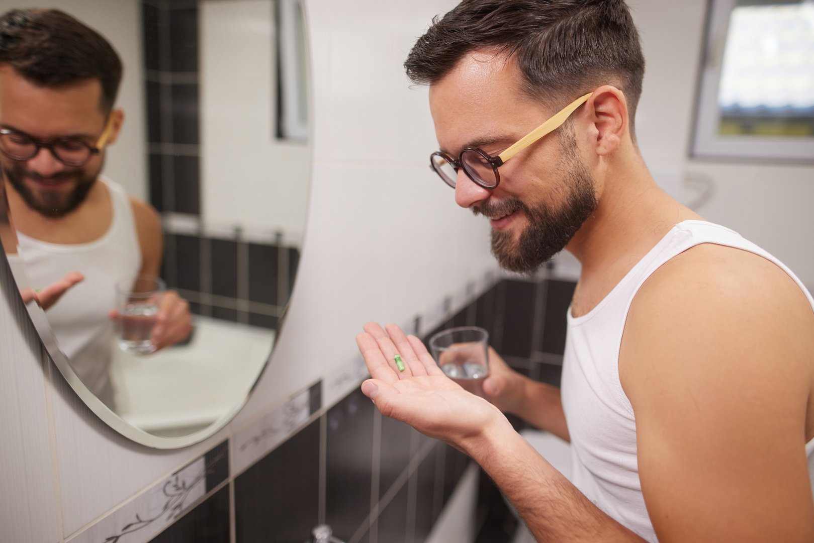 Man holding a green capsule and a glass of water, preparing to take medication