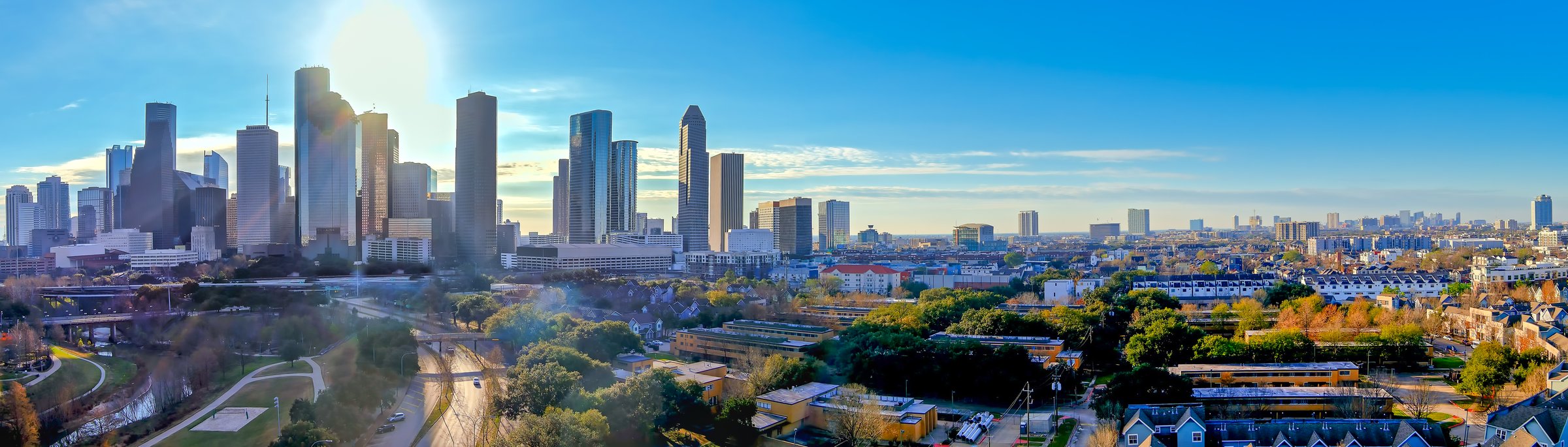 Aerial Panoramic View of the Houston Texas Skyline with a bright blue sky, the sun rising and autumn colors in the treetops.