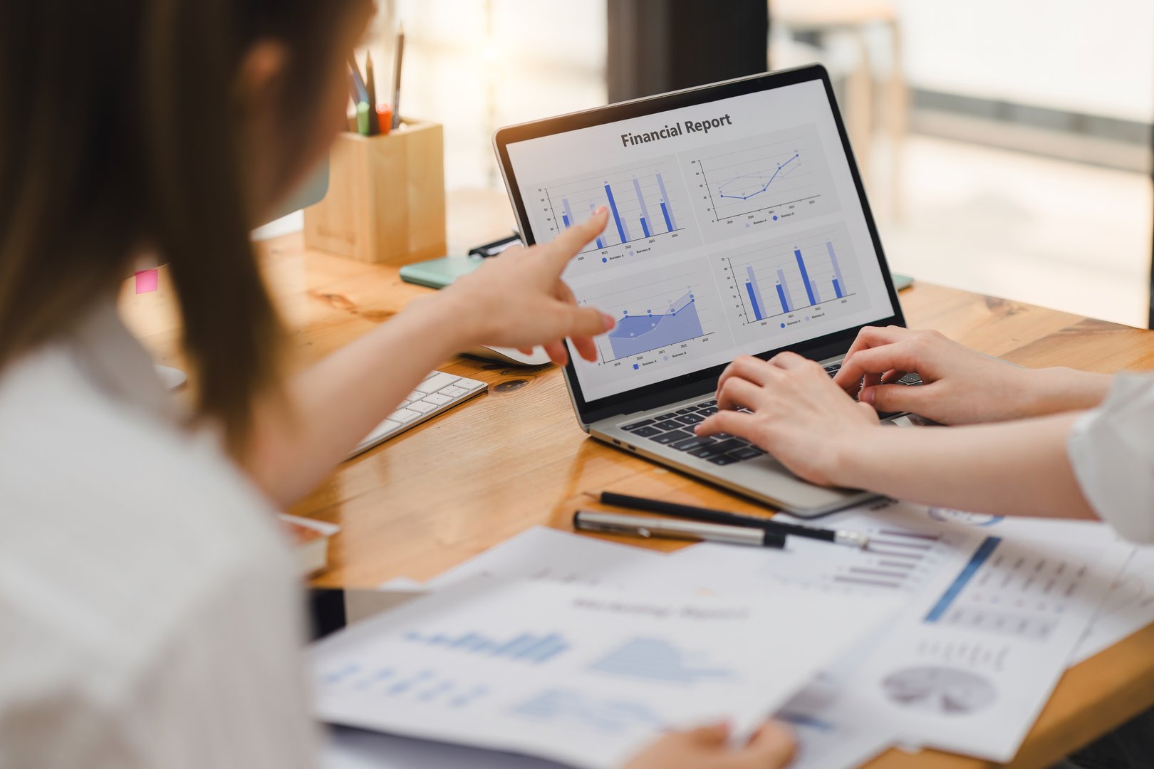 Two colleagues analyzing a financial report with bar and line graphs on laptop at office