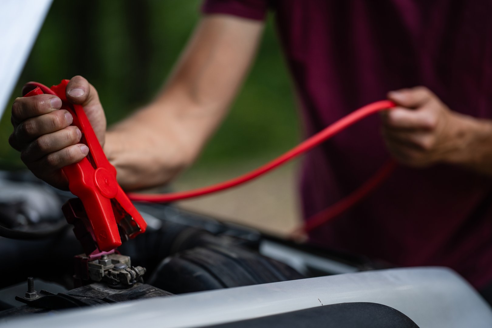 Close-up of hands connecting jumper cables to a car battery, delivering emergency power during a roadside breakdown situation