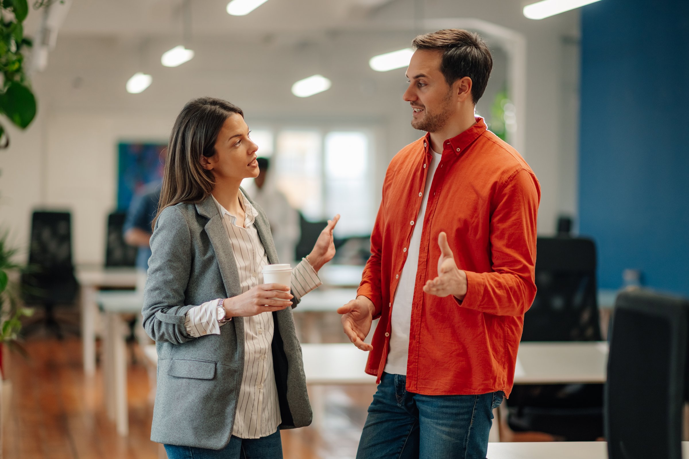 Two young businesspeople are discussing work-related topics during their coffee break in a modern office setting