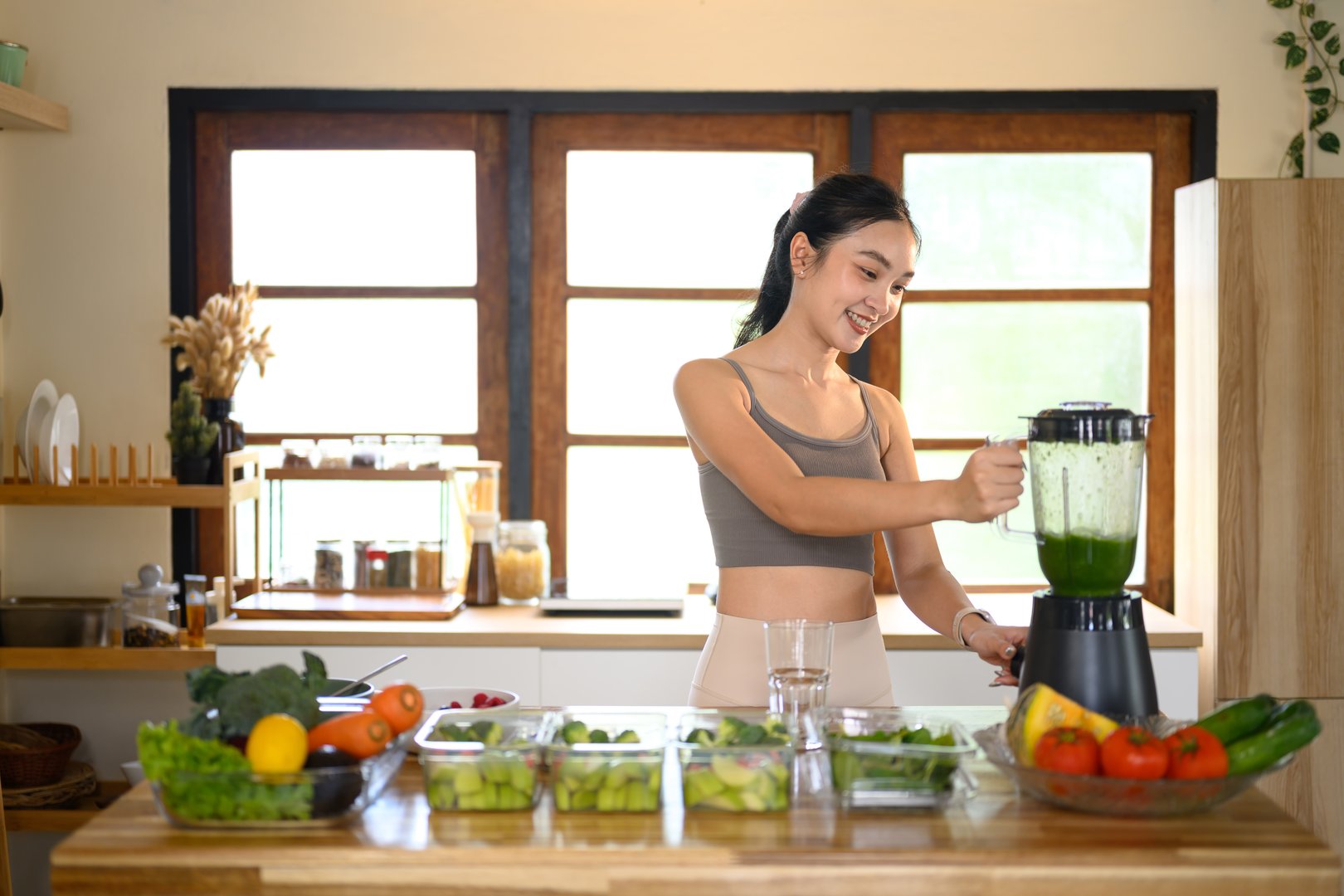 Young woman in activewear preparing a fresh vegetable smoothie for a balanced diet.