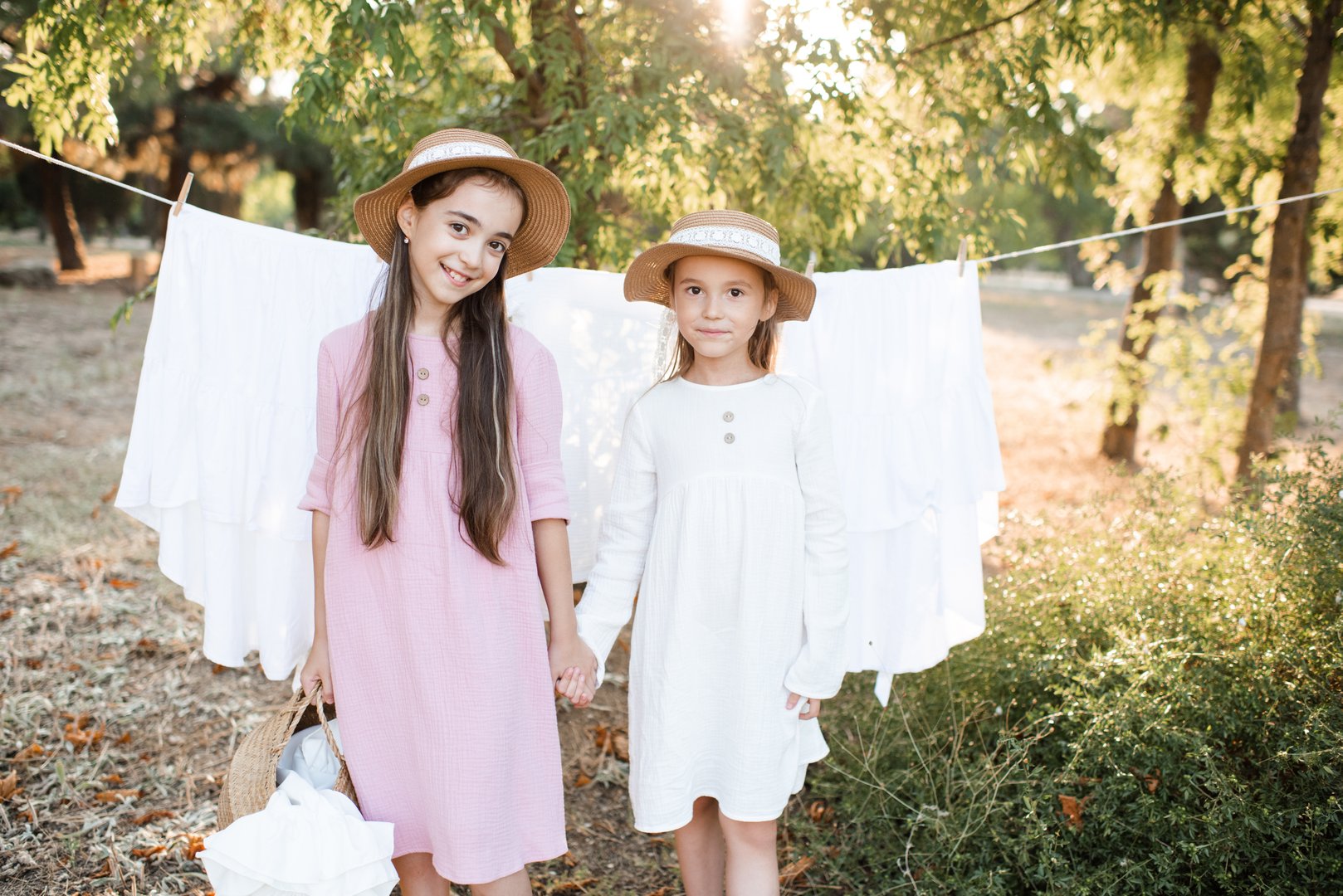 Two child girls playing having fun hanging white bed sheets on rope outdoor. Childhood. Friendship.