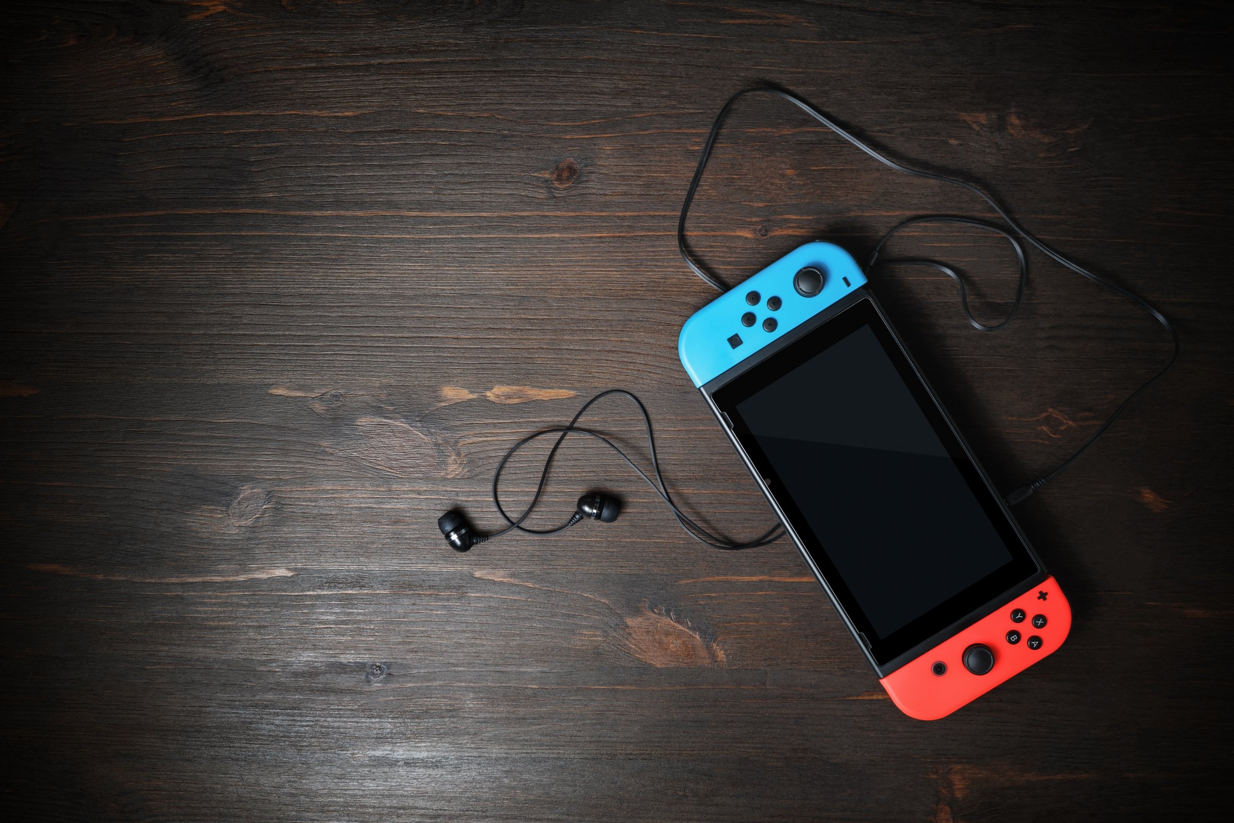 Minsk, Belarus - May 07, 2020: Nintendo Switch game console with black screen and bright joy-con controllers on wood table background. Copy space for text. Top view. Flat lay.