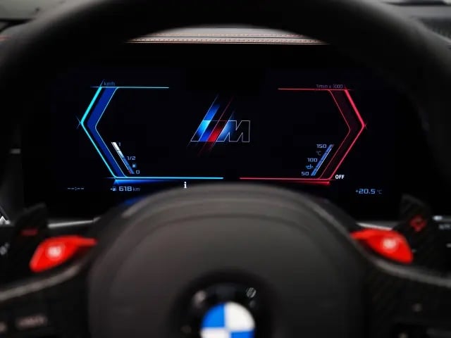 Close-up of a car dashboard featuring a digital display with a BMW M logo, speedometer, and tachometer.