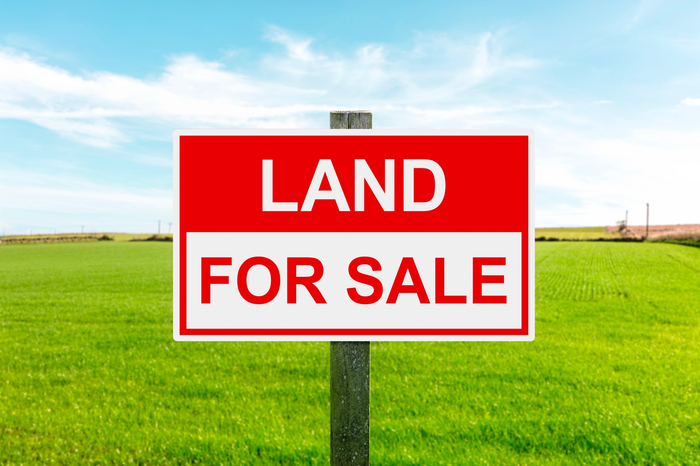 Land for sale sign in green grass field for housing development and construction background