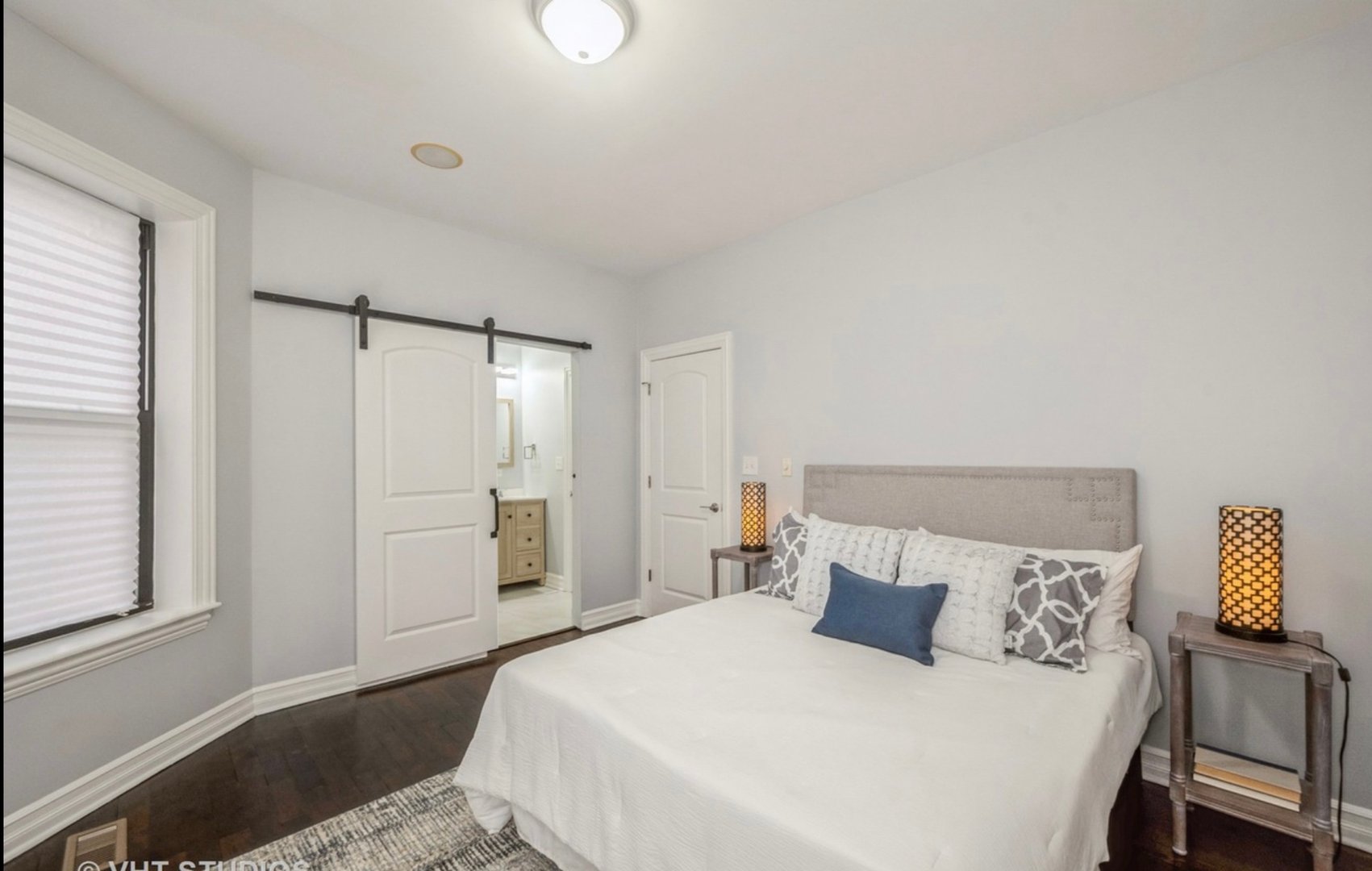 Minimalist bedroom with a white bed, dark wood floor, sliding barn door, and tall lamps on side tables.
