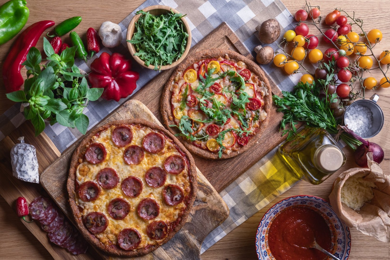 Making pizza with salami, cheese, sauce, tomatoes, vegetables and fresh herbs on wooden background
