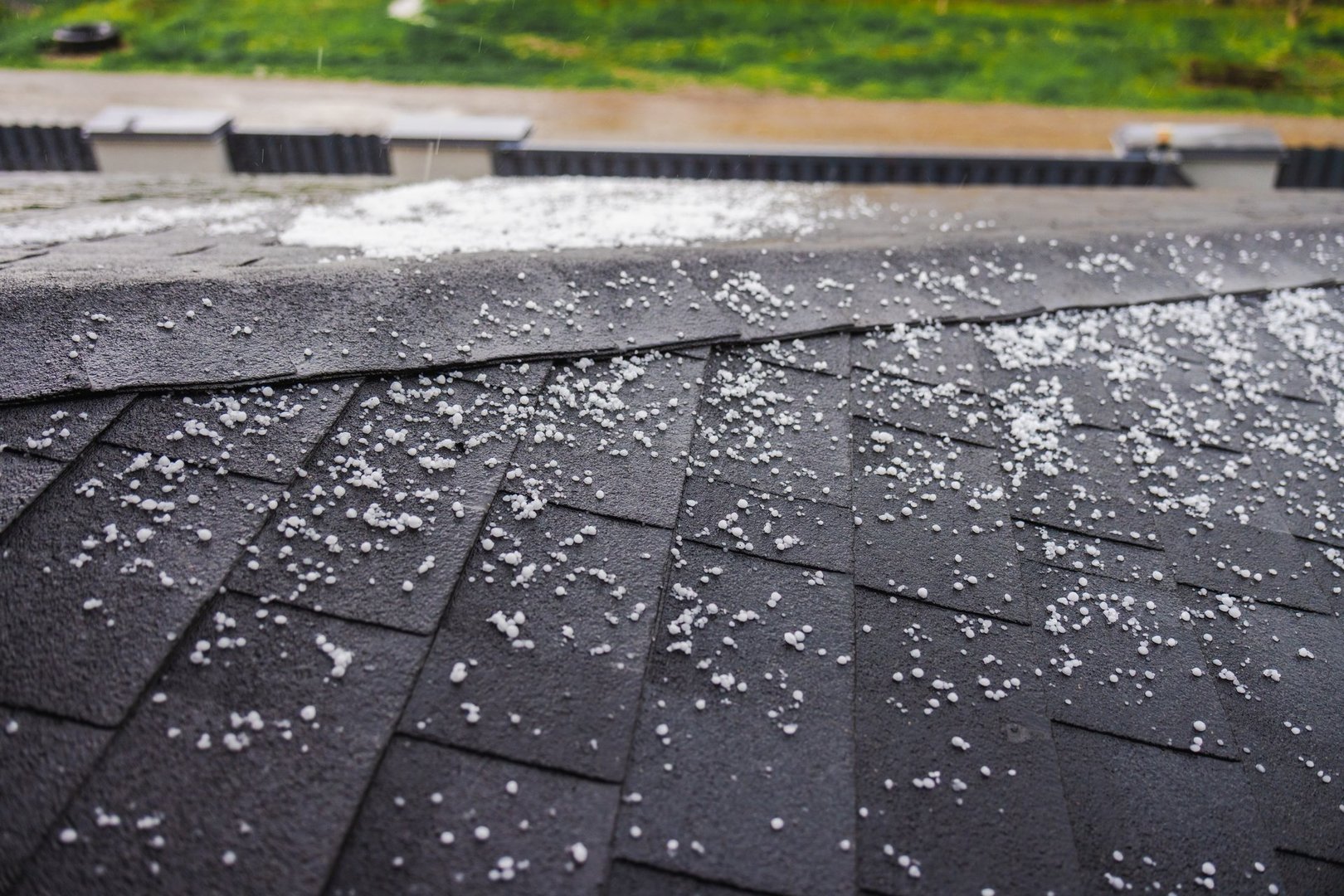 Dark shingled roof covered with scattered small hailstones during a hailstorm