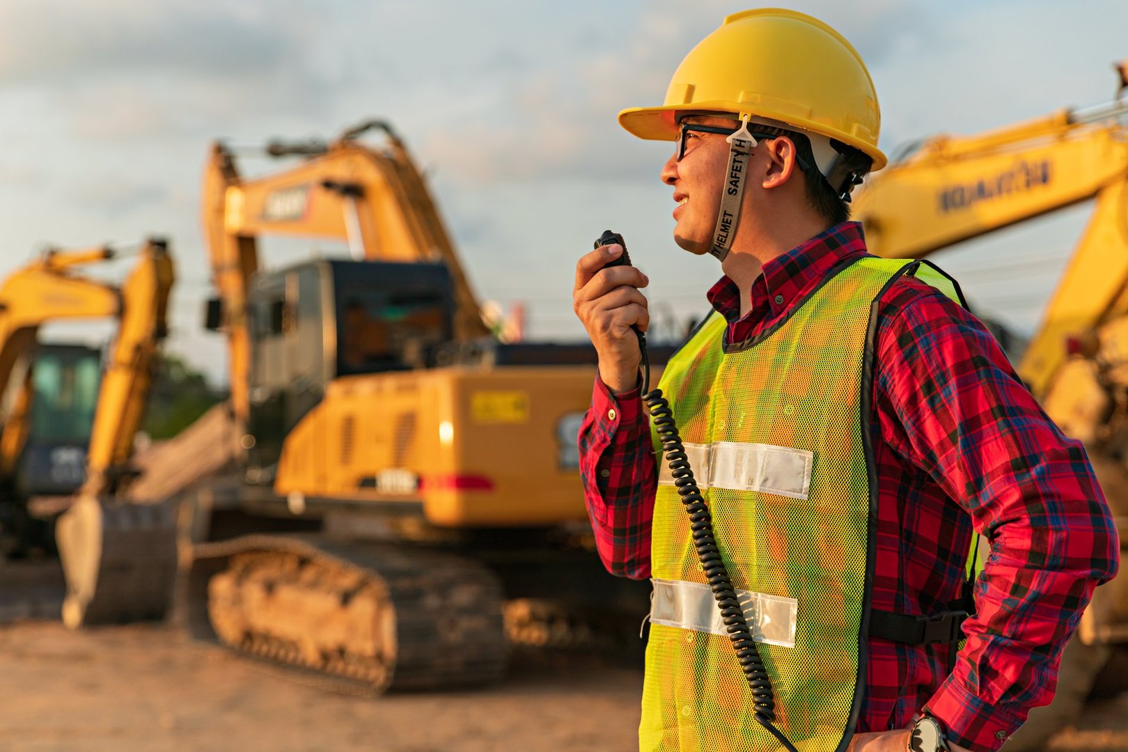 Asian engineers use walky talky with team for earthmoving project by excavator. foreman use laptop for construction project heavy digger. machinery and equipment for worker industrial.